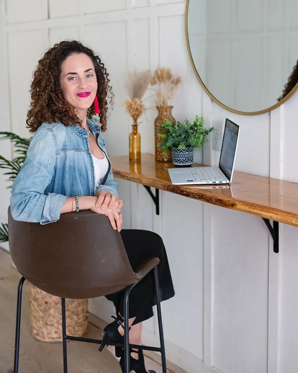 Career break coach Katrina McGhee relaxed on a leather stool in her bright home office with laptop and plants