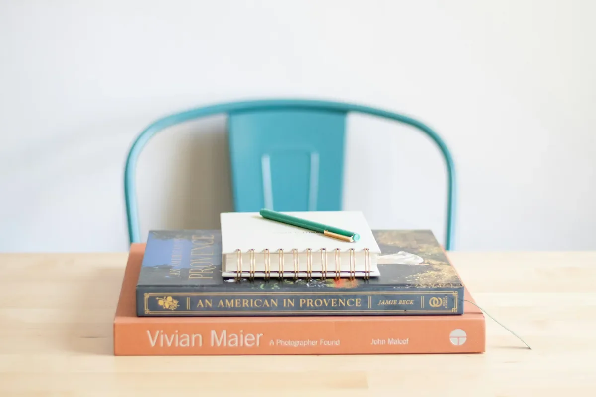 Stack of travel and photography books with a spiral notebook and pencil on a wooden table, evoking career break planning and exploration