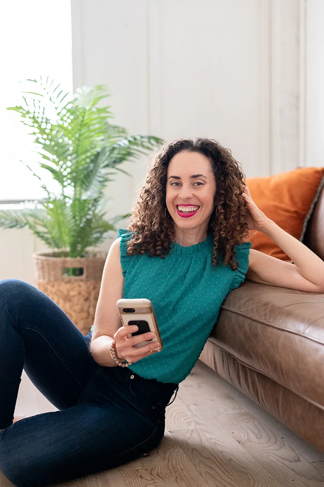 Katrina McGhee sitting on floor holding phone, smiling beside a leather sofa
