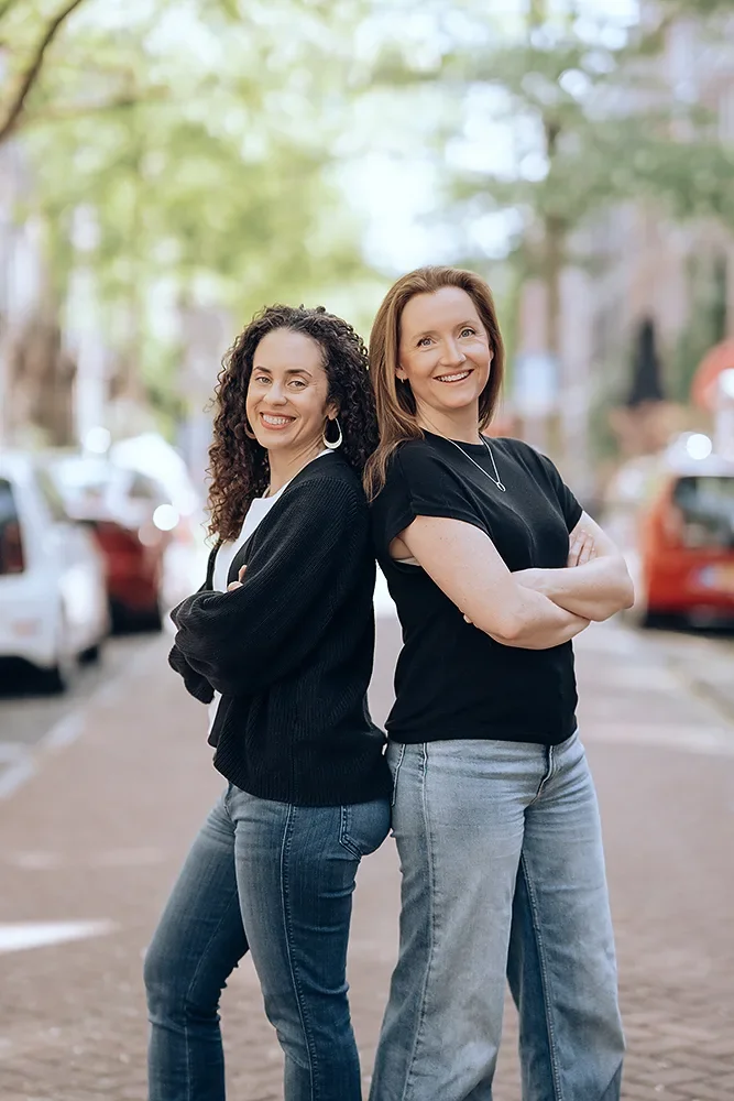 Two BreakSpace career break coaches standing back to back, smiling upward confidently on a sunny street