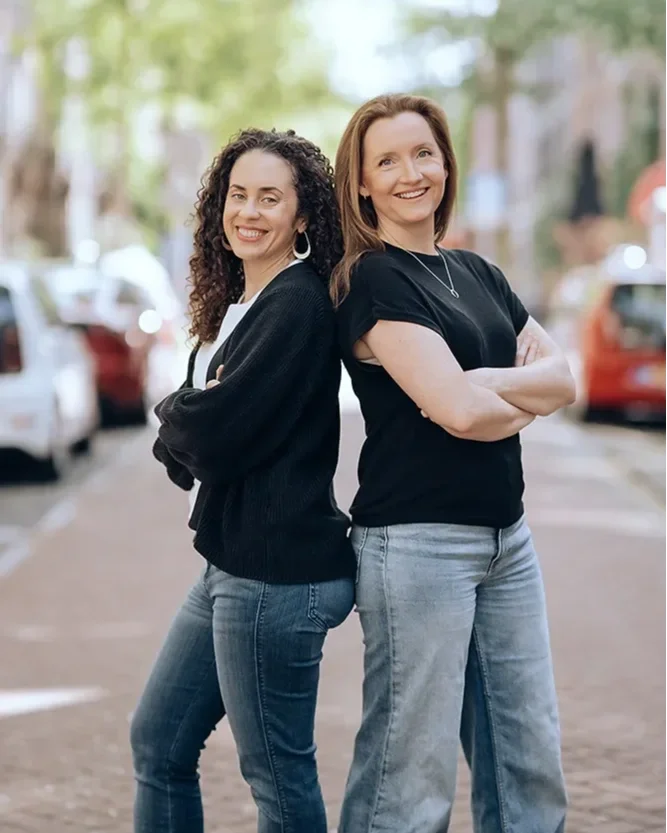 Two BreakSpace career break coaches standing back to back, smiling upward confidently on a sunny street