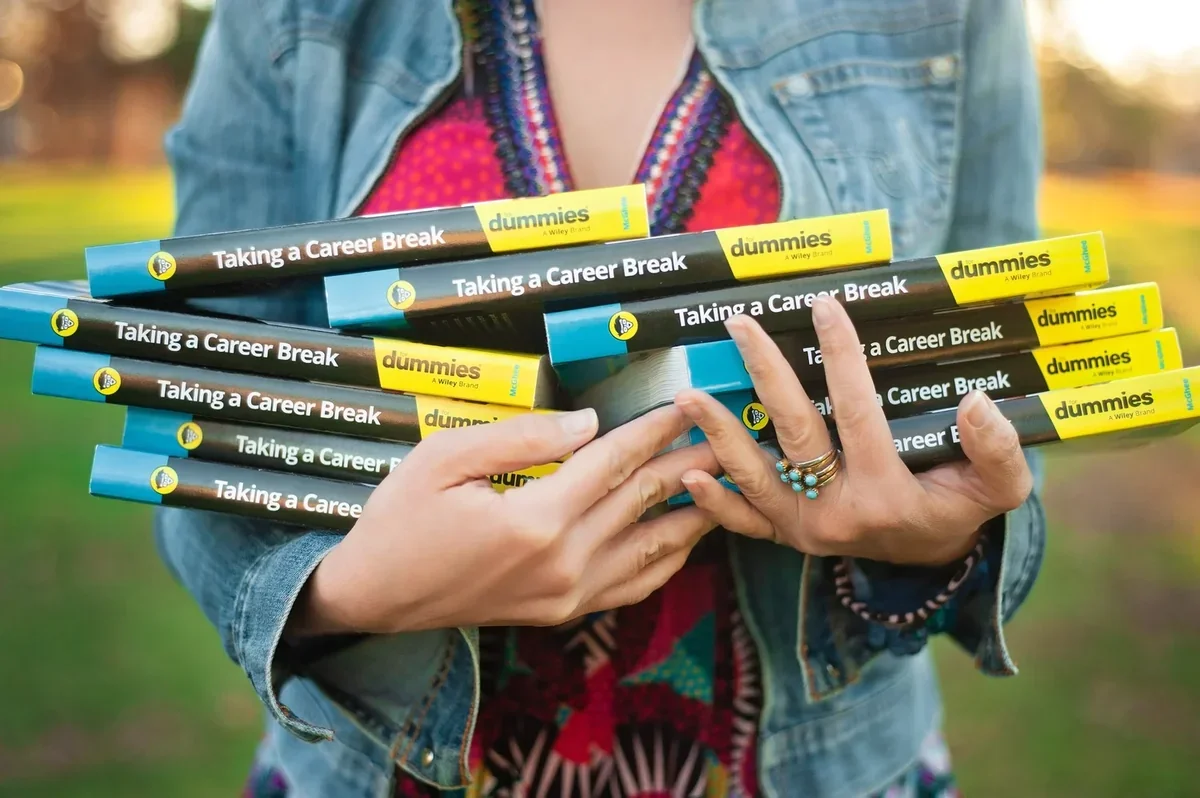 Stack of Taking a Career Break For Dummies books held in two hands, denim jacket and colorful top in background