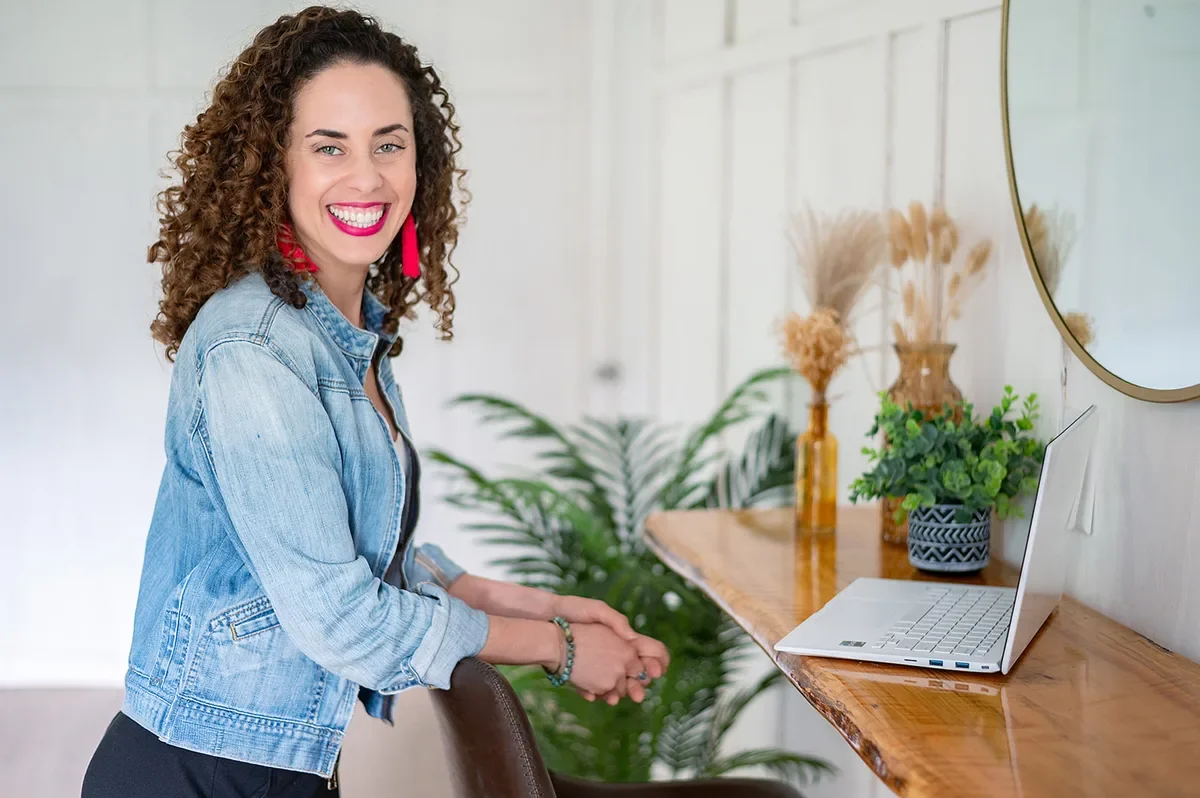 Katrina McGhee career break coach laughing beside laptop at wooden desk with plants