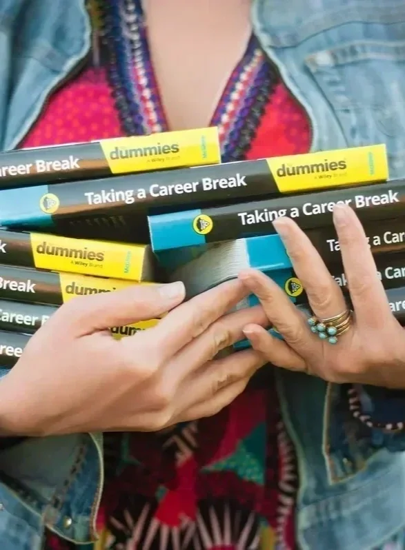 Stack of Taking a Career Break For Dummies books held in two hands, denim jacket and colorful top in background