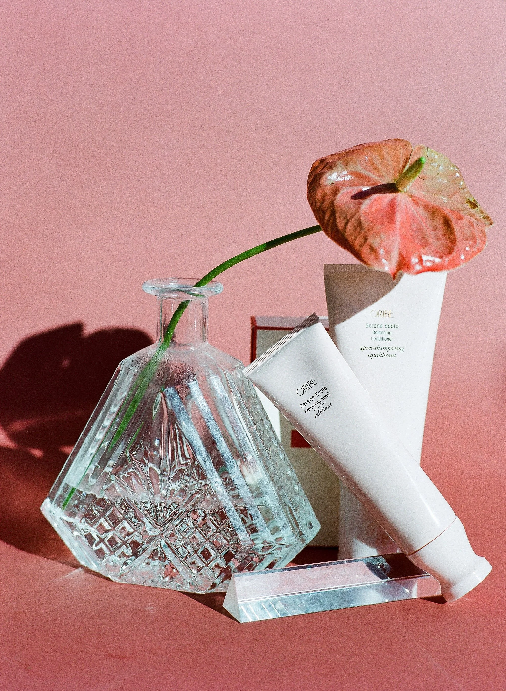 Oribe Serene Scalp products styled with textured glass vase and pink anthurium flower on blush backdrop.