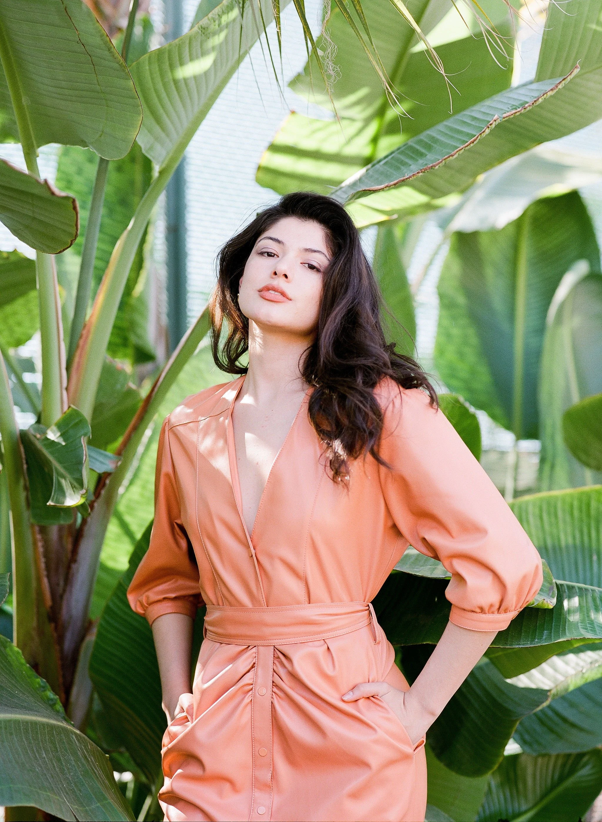Brunette model in a peach dress posed among tropical leaves for an Oribe luxury haircare campaign.