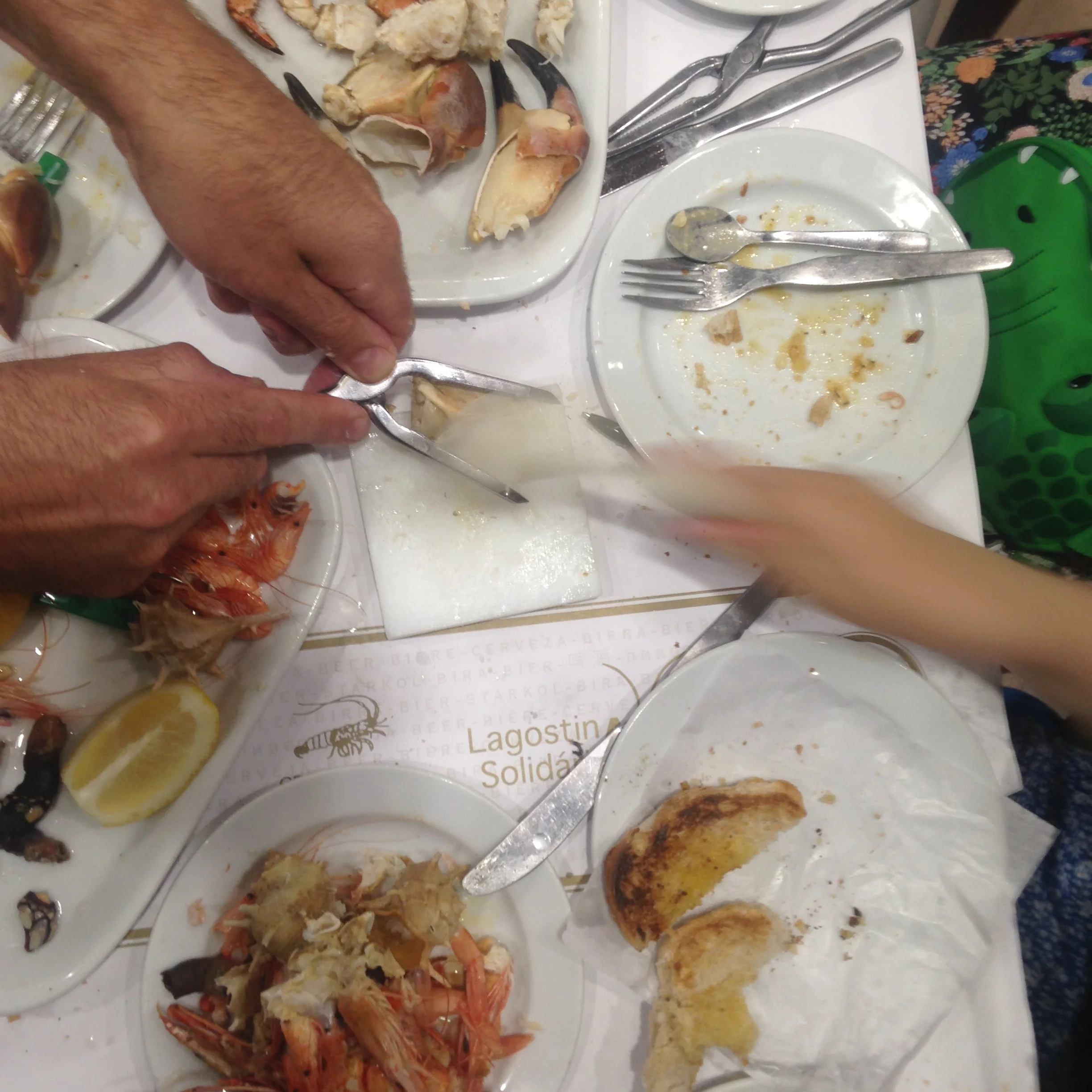 People eating seafood, including shrimp and crab, with utensils and tools on white plates and table.