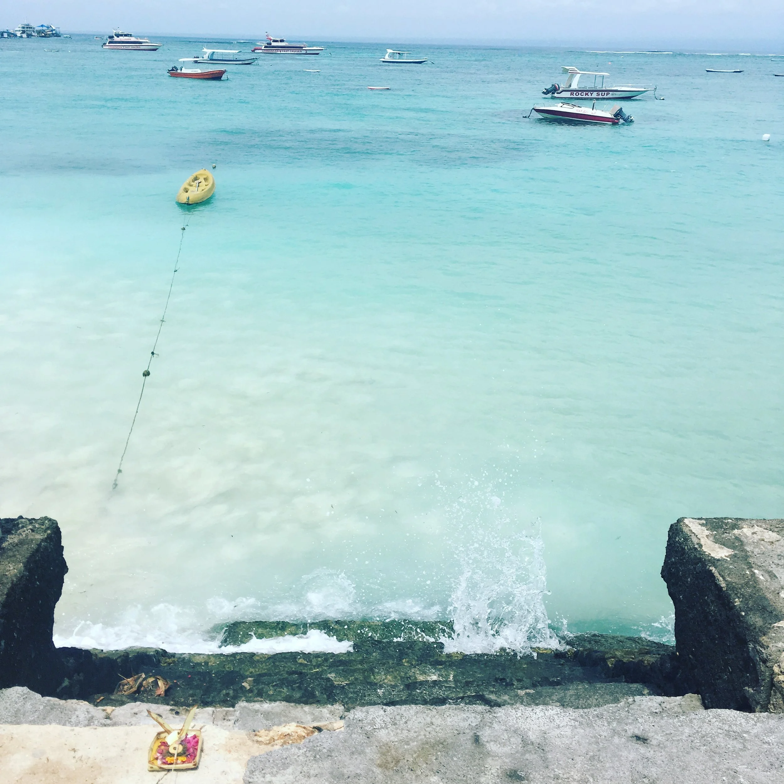 Tropical beach scene with turquoise water, boats anchored in the distance, and a small yellow kayak tied offshore.