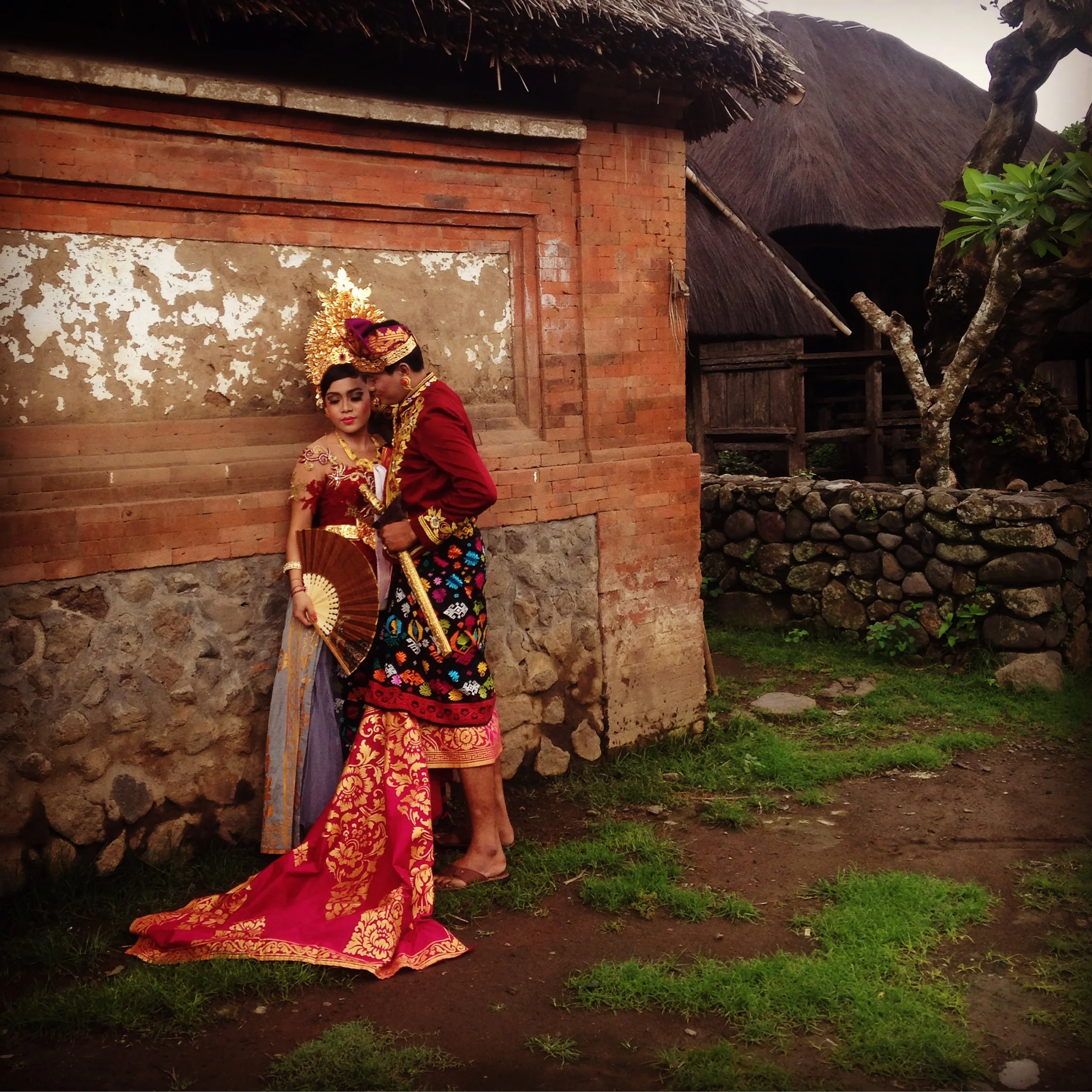 Couple in traditional Indonesian attire embracing beside a rustic wall