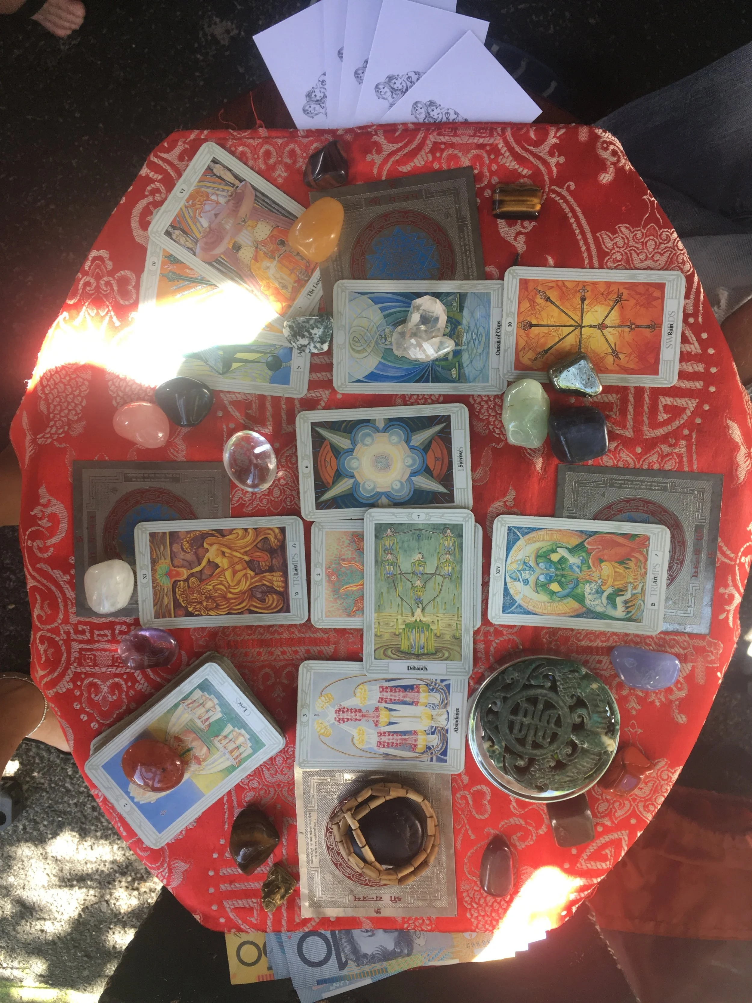 Tarot card spread on a red patterned cloth with various crystals and stones placed around them.