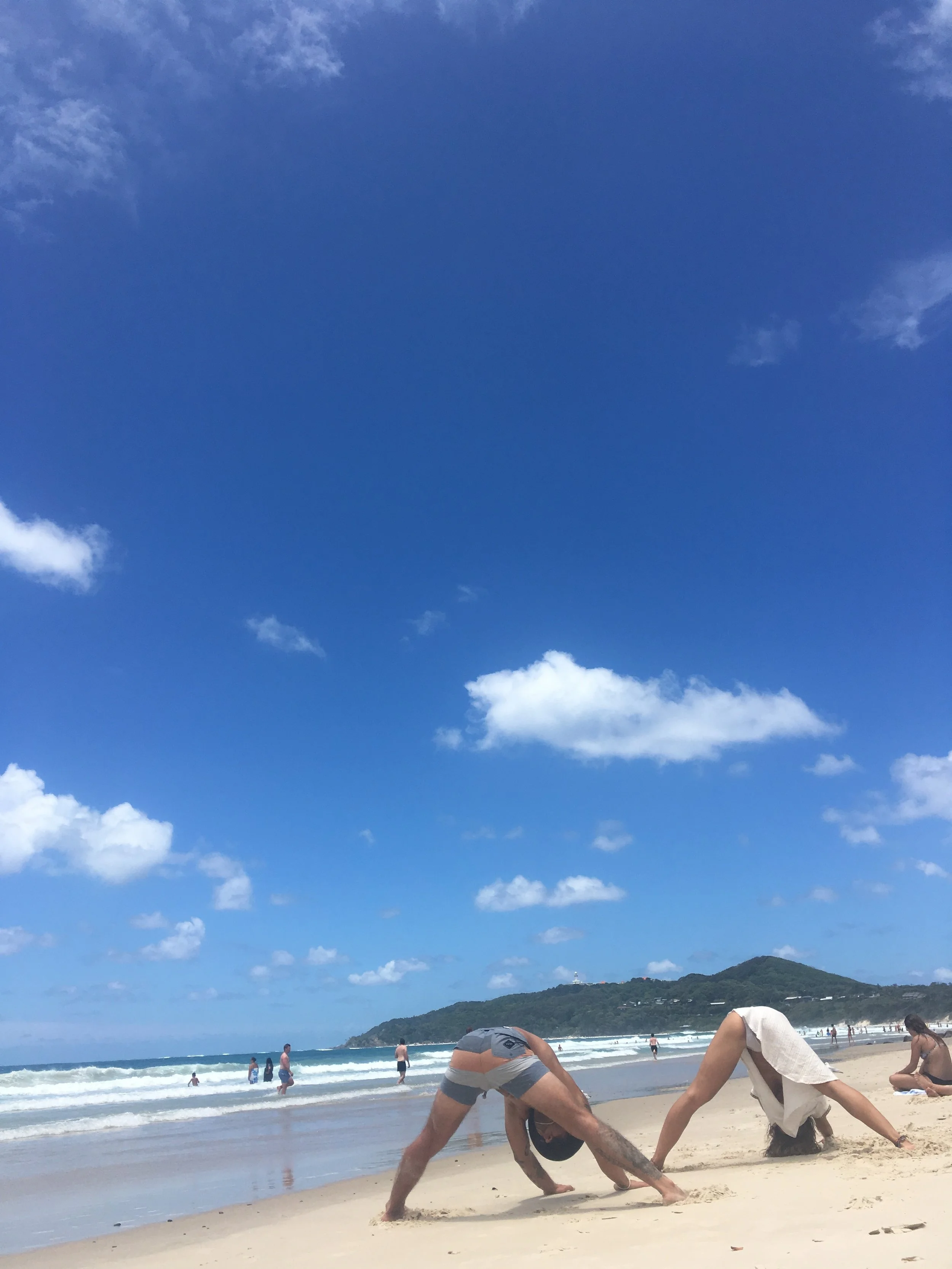 People stretching on a sandy beach with a bright blue sky and ocean waves in the background.