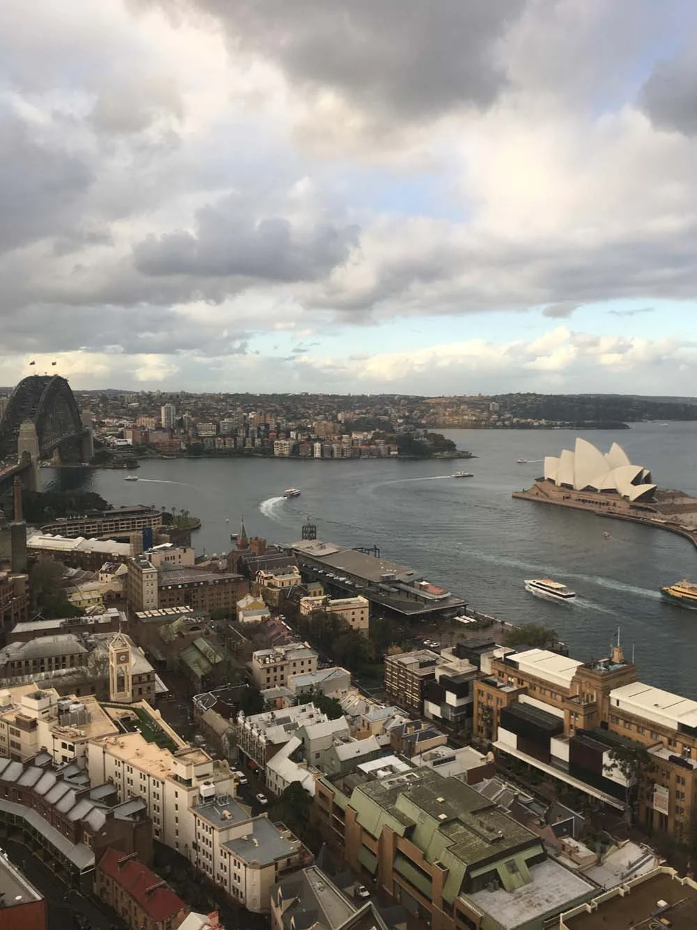 Aerial view of Sydney Harbour with the Sydney Opera House and Sydney Harbour Bridge, surrounded by urban landscape and water.