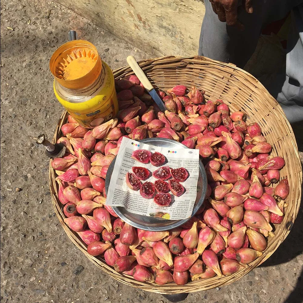 Basket of fresh prickly pear fruits with a plate of sliced pieces and a jar of turmeric nearby.