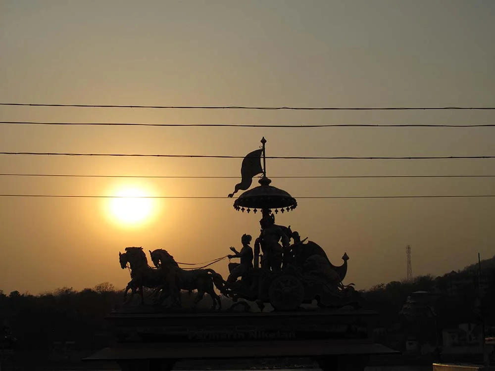 Silhouette of a chariot statue with horses and warriors at sunset with power lines in the foreground.