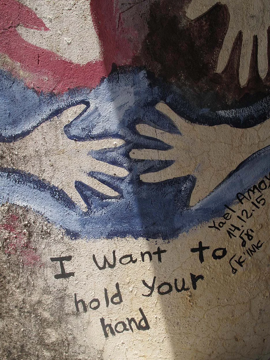Street art mural featuring abstract hands in red, blue, and black, with text "I Want to hold Your hand." Signed by Yael Aram on 14.12.15.