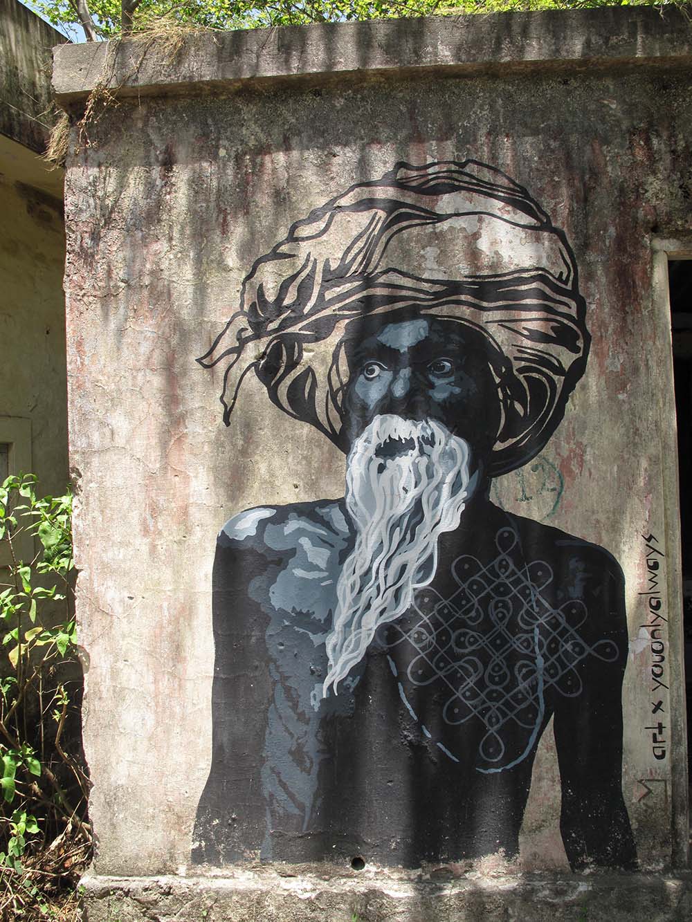 Street art mural of an elderly man with a long white beard and turban on a textured wall.