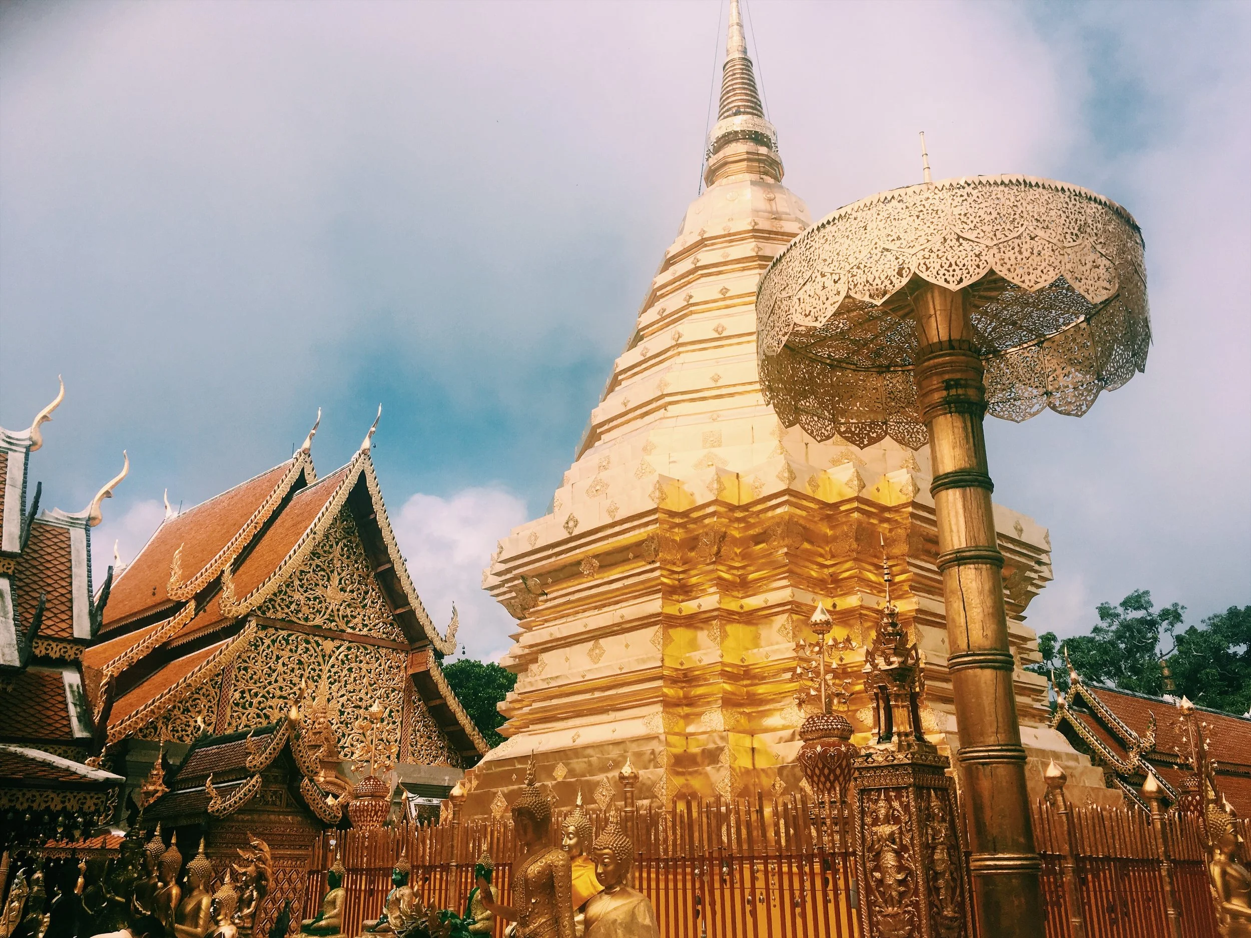 Golden Buddhist temple with ornate rooftops, a golden stupa, and elaborate decorations under a blue sky.