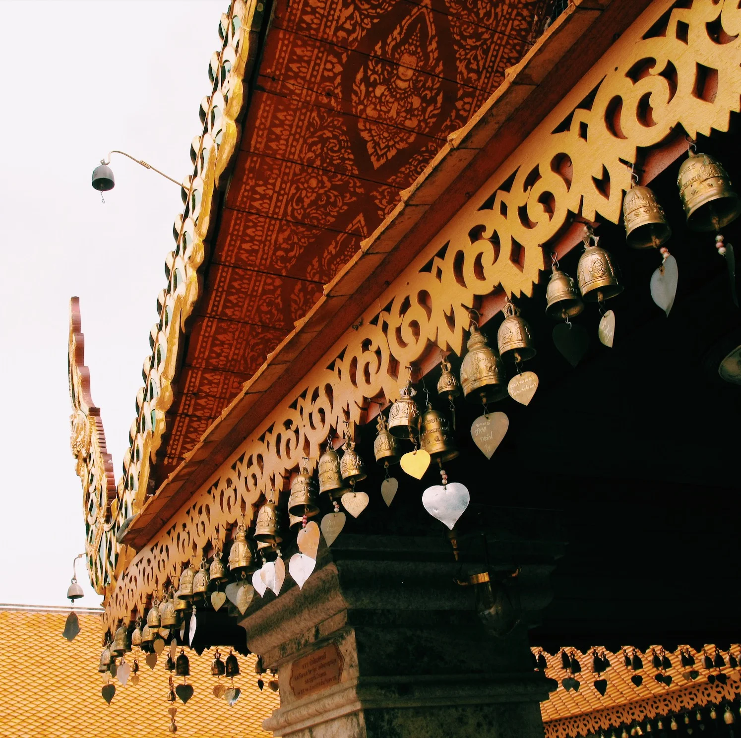 Decorative temple roof with gold ornamentation and hanging bells, featuring intricate patterns and heart-shaped tags.
