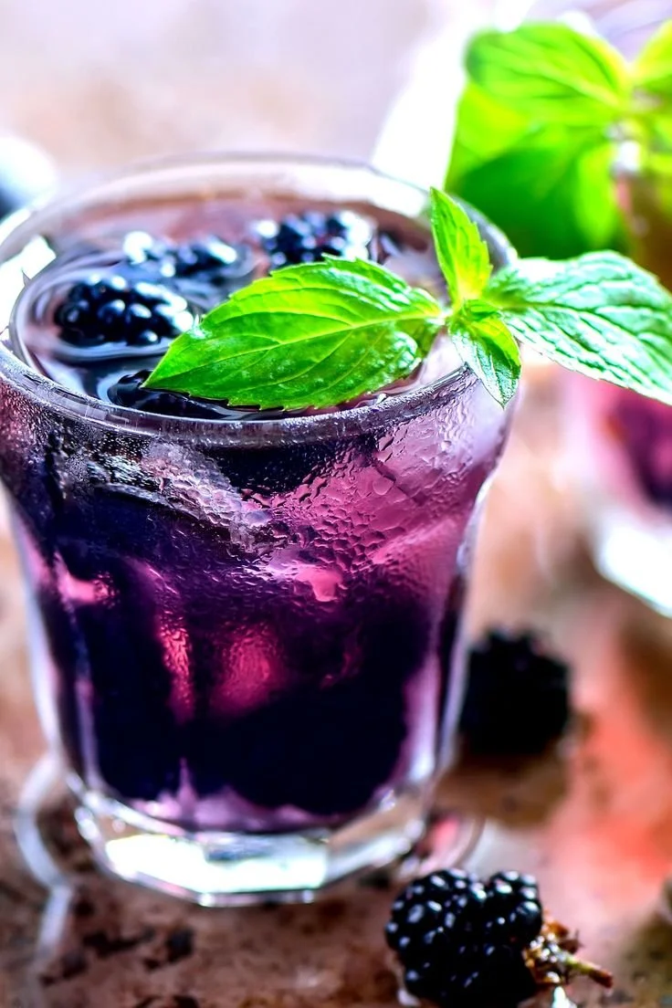 Glass of blackberry beverage garnished with mint leaves
