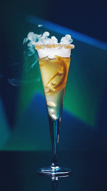 A cocktail in a tall glass with lemon slices, ice, and frothy topping, with smoke or vapor rising from it.