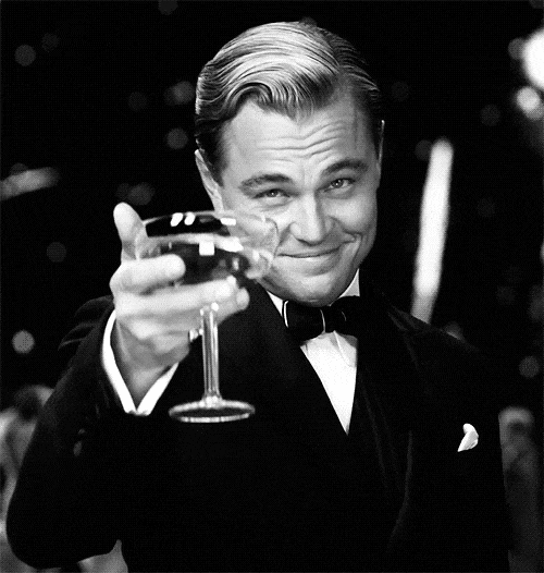 A man in a tuxedo holding a glass of wine, smiling and toasting.