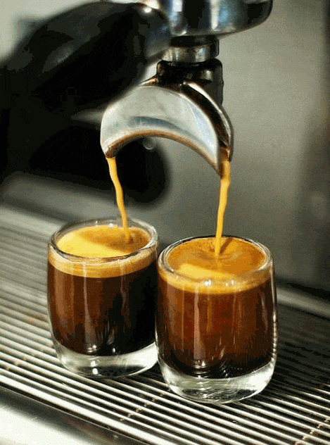 Two espresso shots being poured into small glasses from an espresso machine.