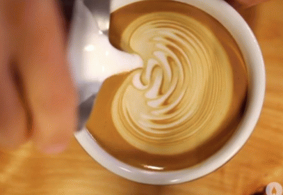 Close-up of a latte coffee with caramel-colored swirls in a white cup on a wooden surface.