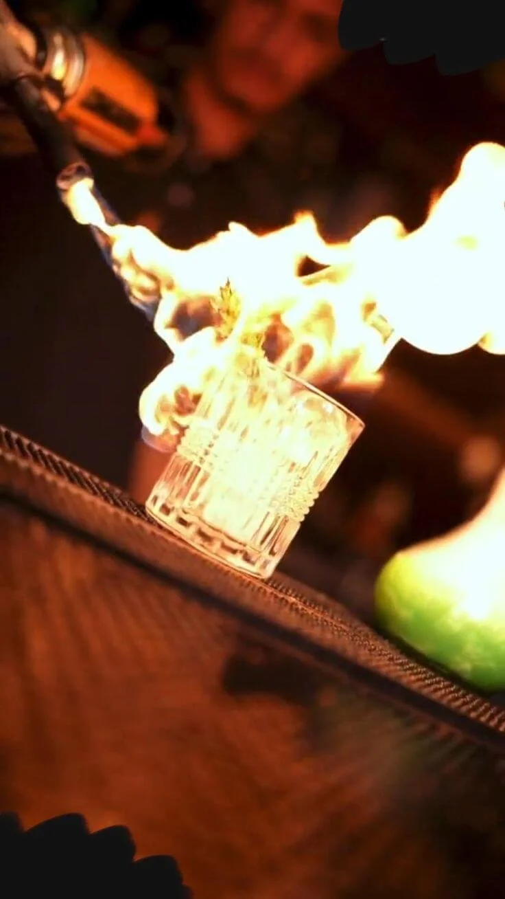 A person holding a torch with a flame directed towards a glass, creating a fire effect.