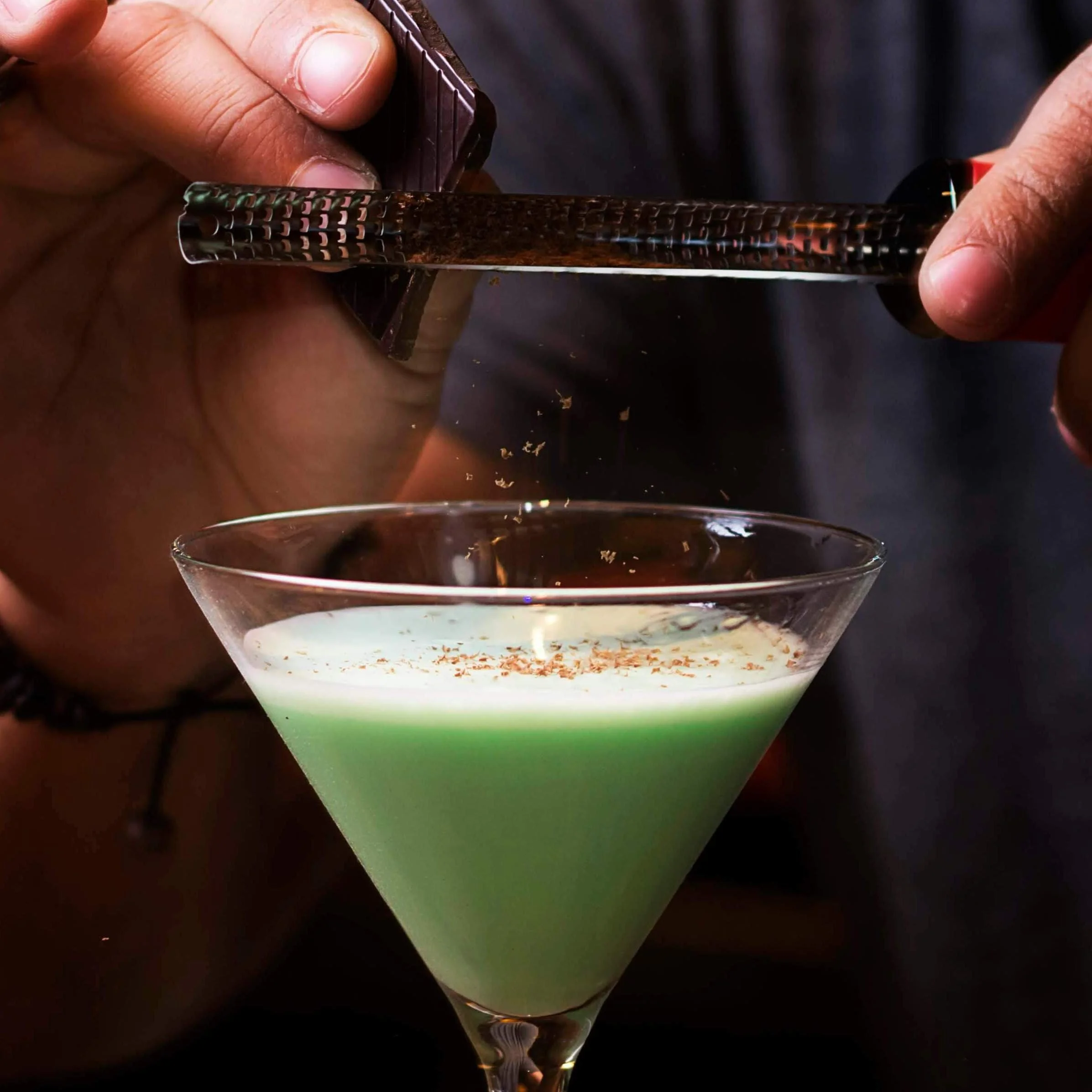 Person garnishing a green cocktail with chocolate flakes.