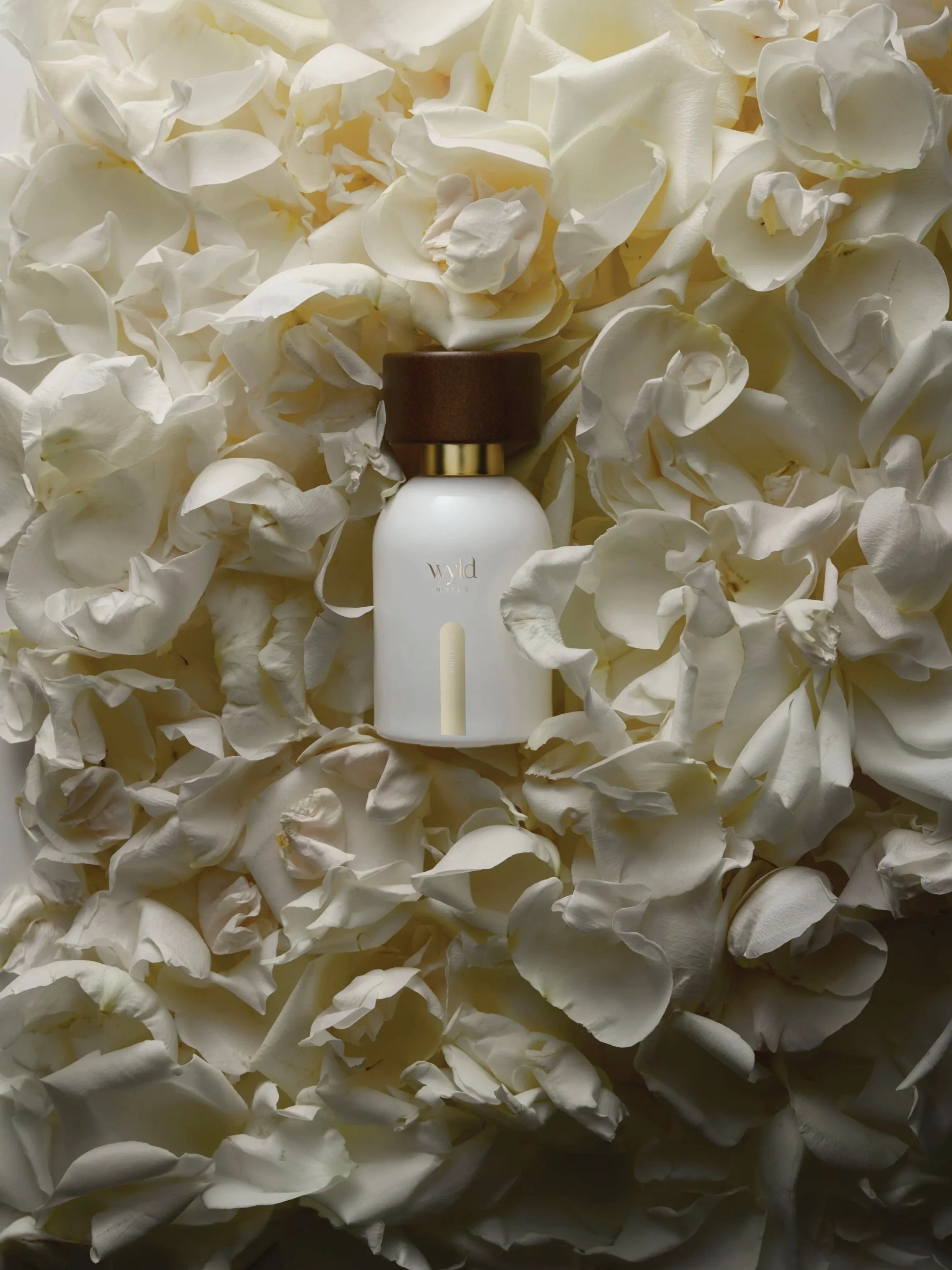 A white perfume bottle with a brown cap placed among white flower petals.