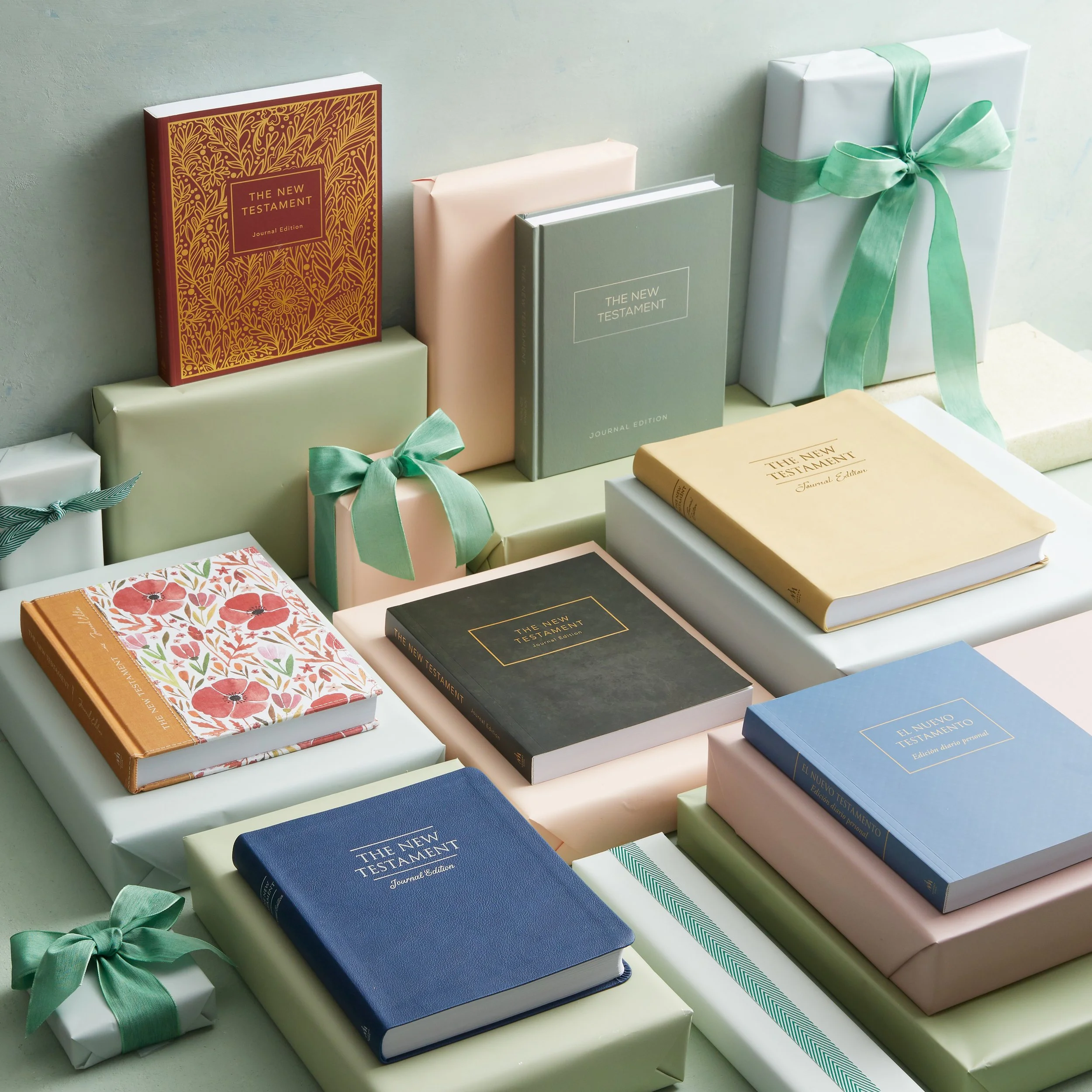Stack of religious books, including Bibles and religious texts, some wrapped as gifts with ribbons, arranged on boxes and a light-colored surface.