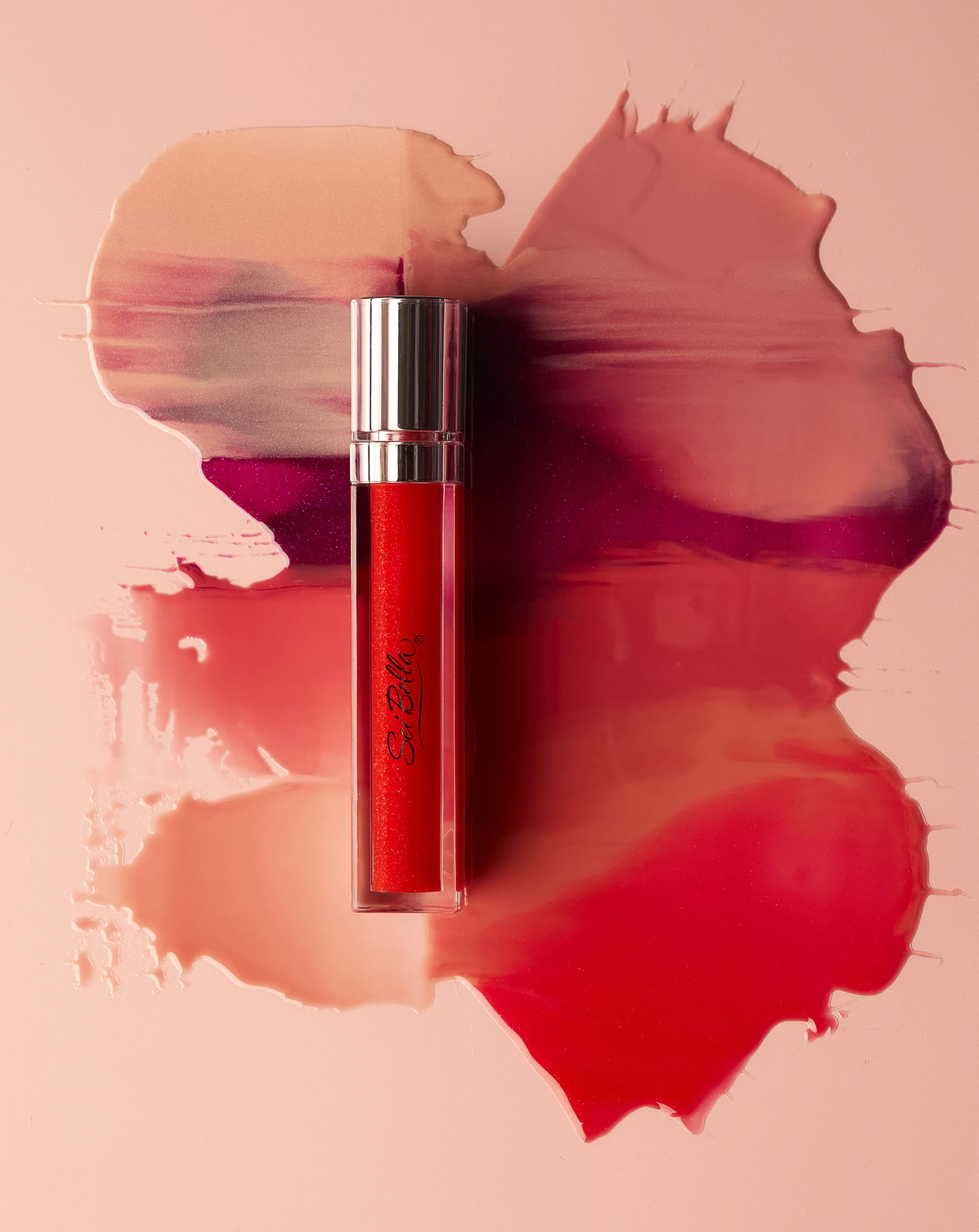 A red lipstick tube with silver accents lies on a pink surface, with smudges of red lipstick and stains spreading outward around the tube.