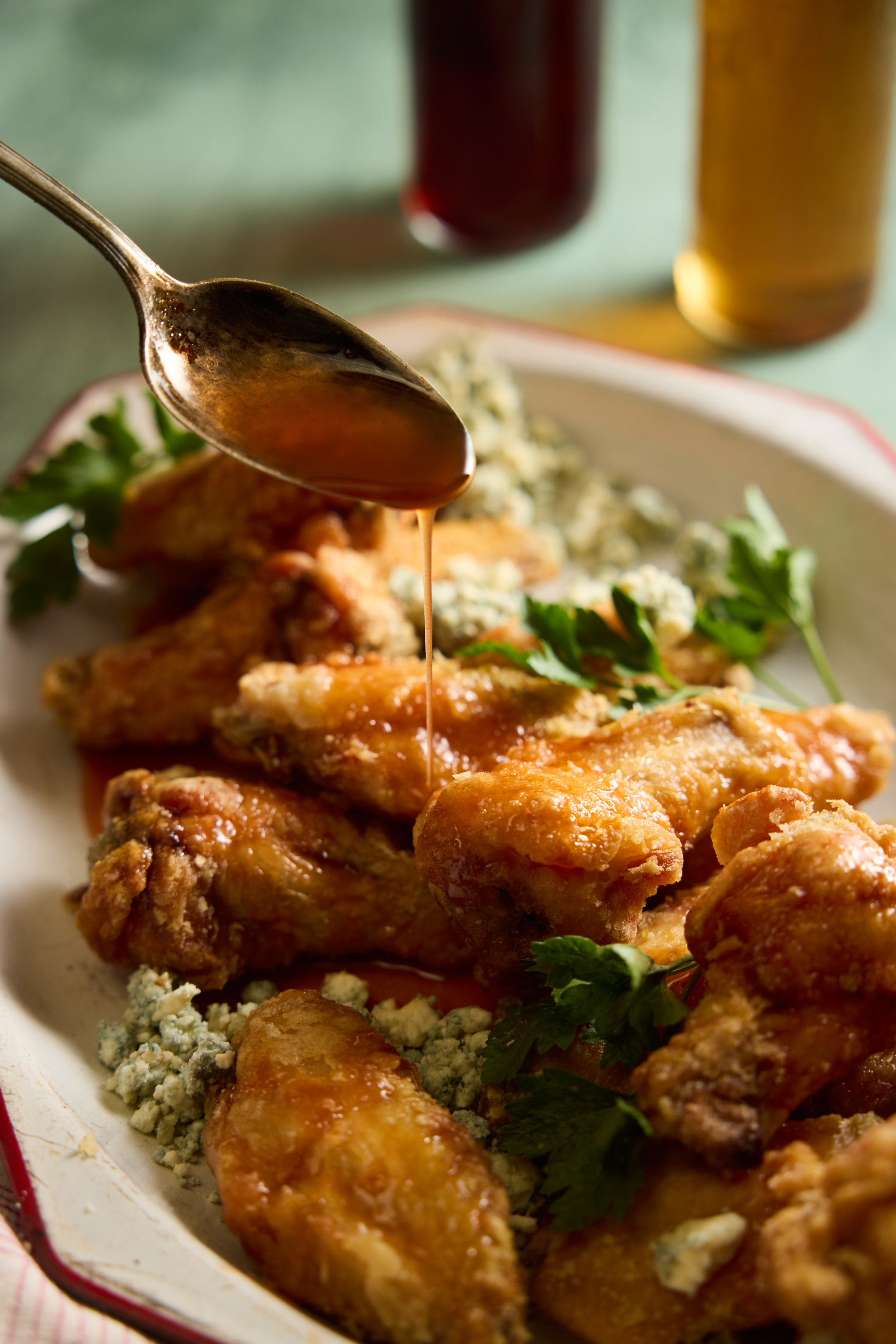 Fried chicken with gravy, blue cheese crumbles, and parsley on a white plate with two drinks in the background.