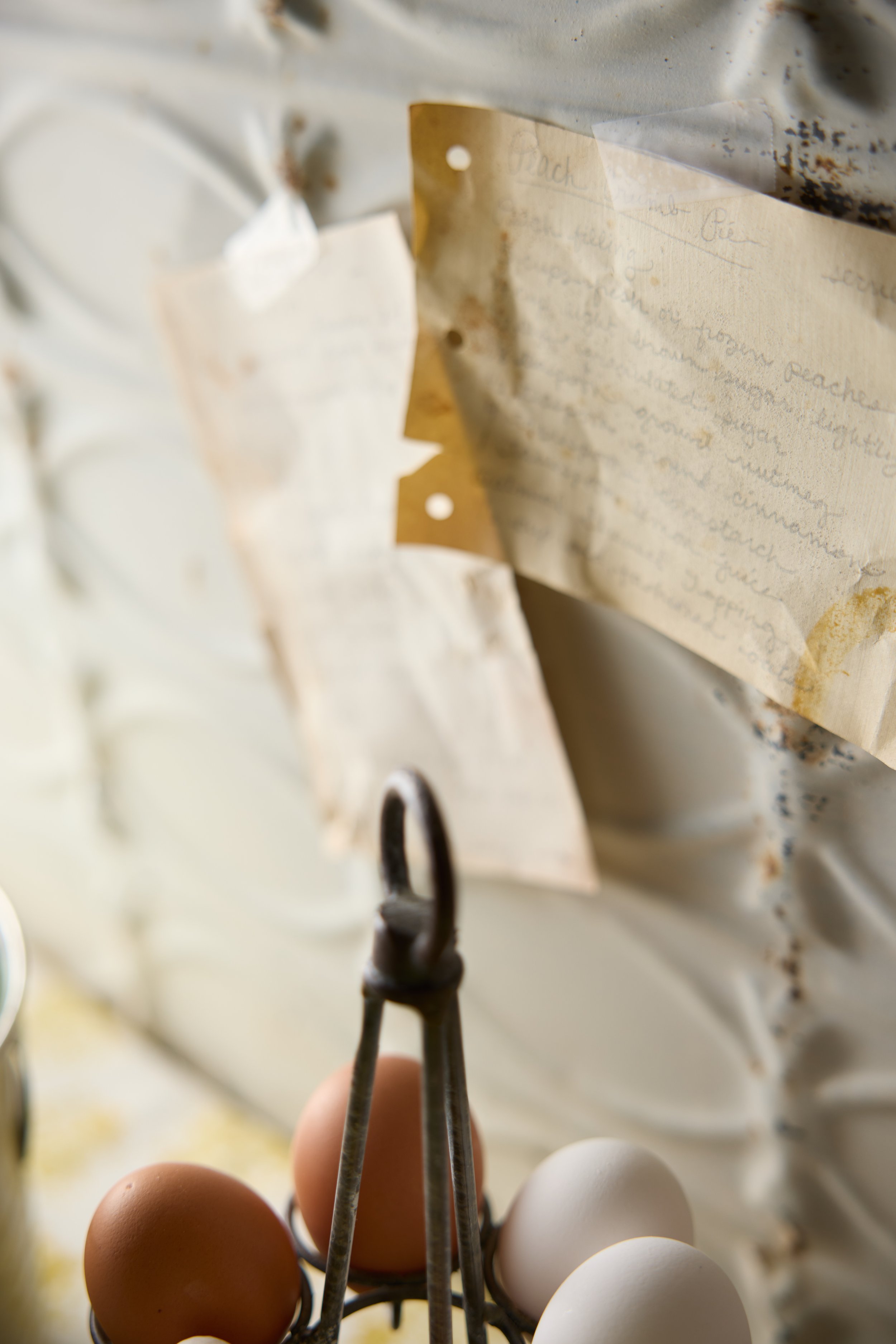 Close-up of a hand holding a metal egg holder with brown and white eggs, with handwritten notes on paper pinned to a wall or board in the background.