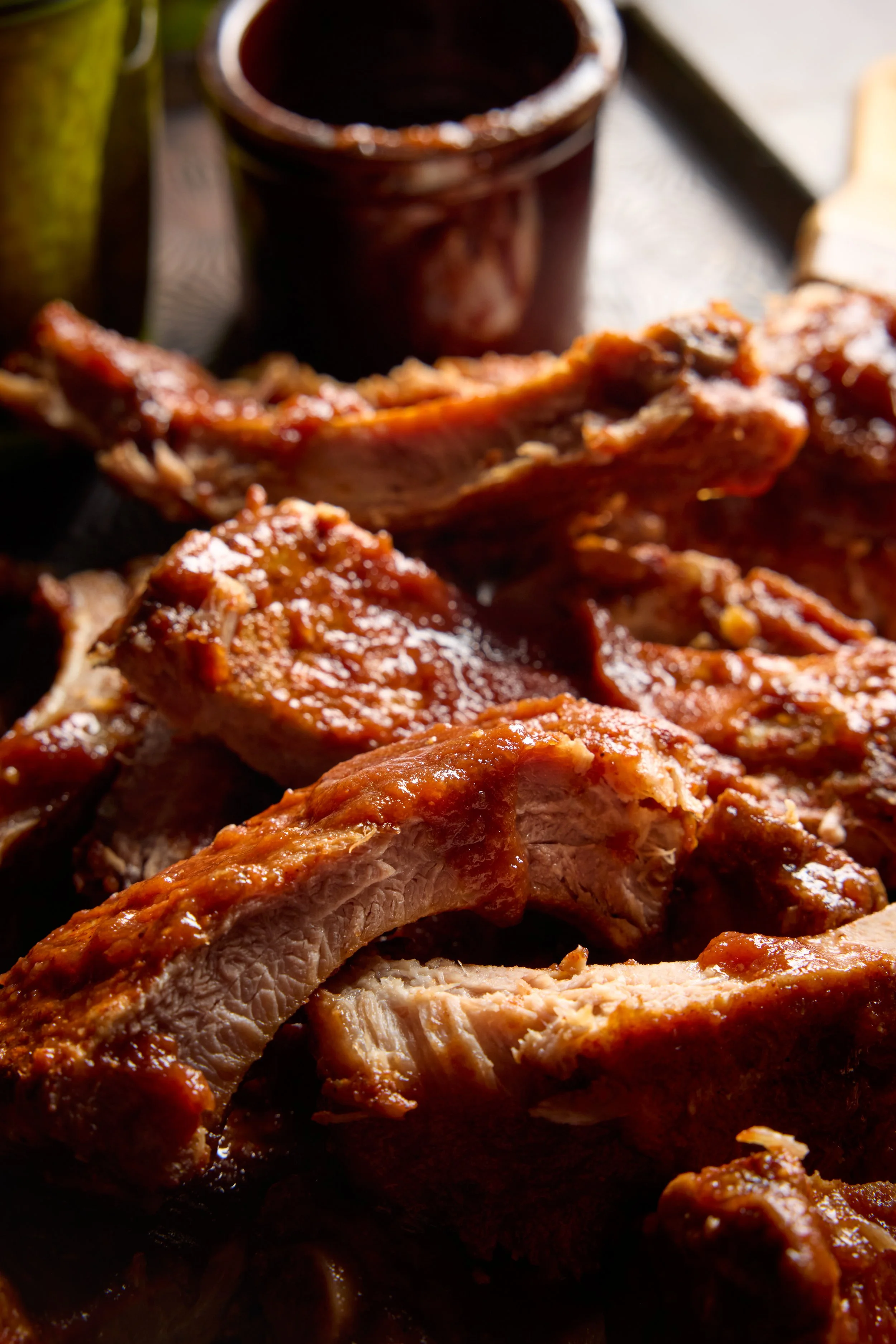 Close-up of grilled pork ribs with barbecue sauce, on a dark surface with a black cup in the background.