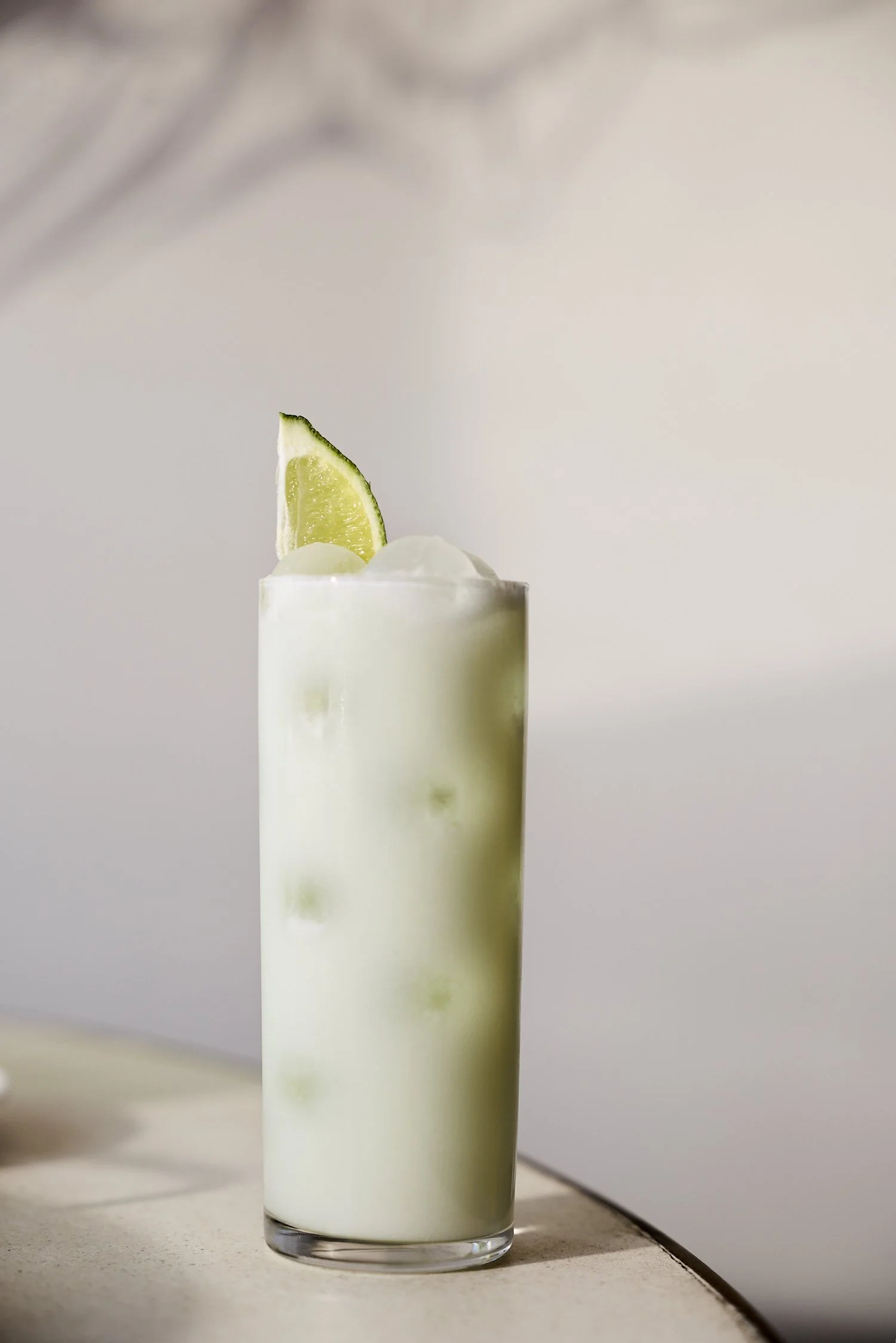 A tall, clear glass filled with a pale green drink, garnished with a lime wedge on top.