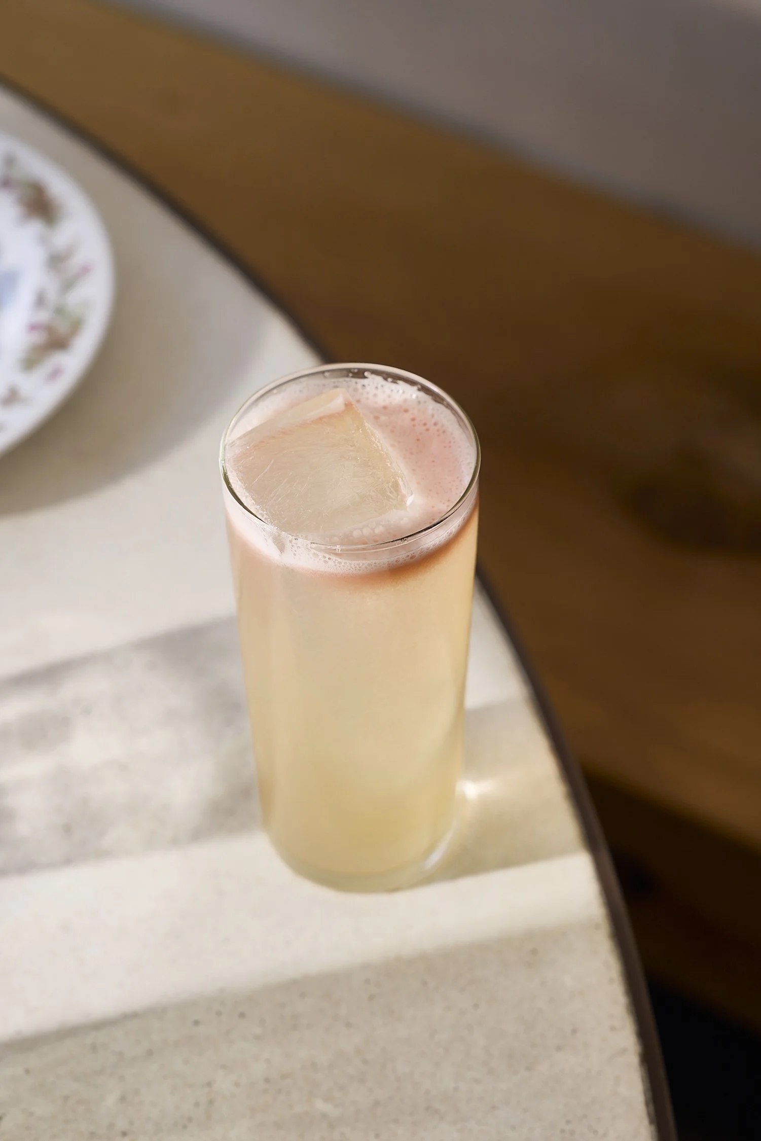 A tall glass of pink beverage with a large ice cube on top, placed on a beige countertop.