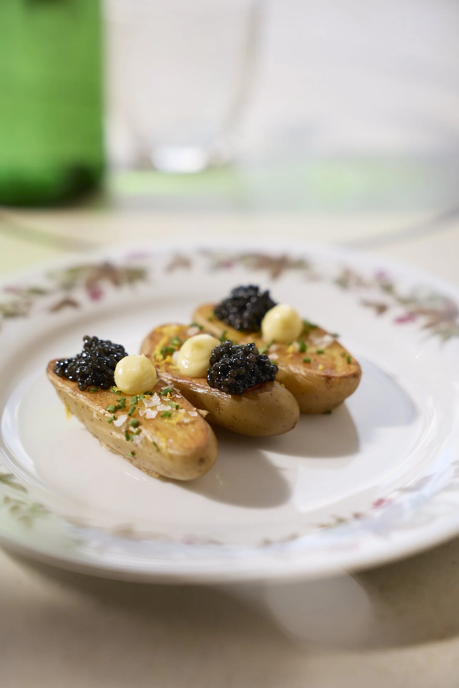 Dish with halved potatoes topped with black caviar, white sauce, and chopped herbs on a floral-patterned plate.