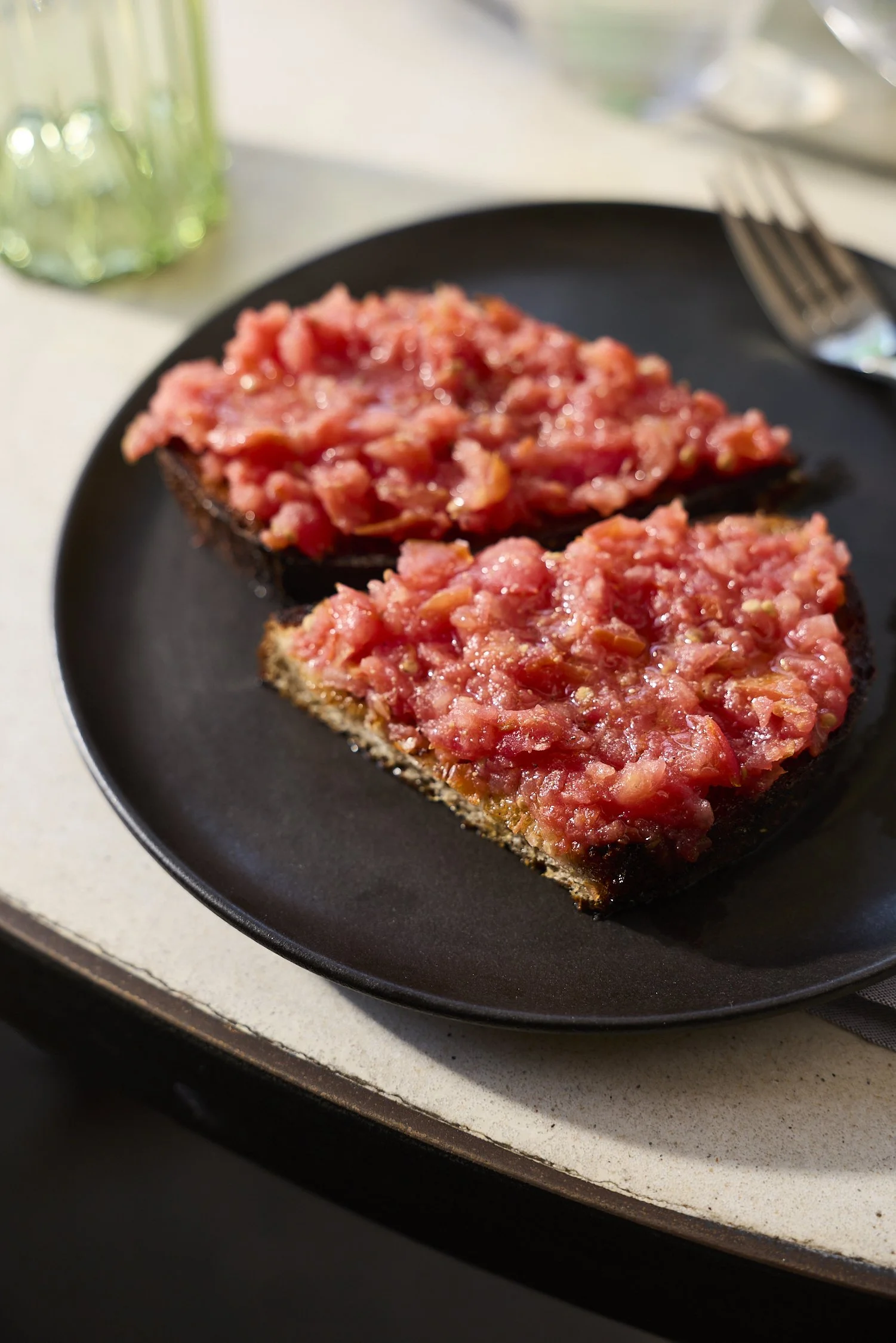 Close-up of toasted bread slices topped with chopped tomatoes on a black plate.