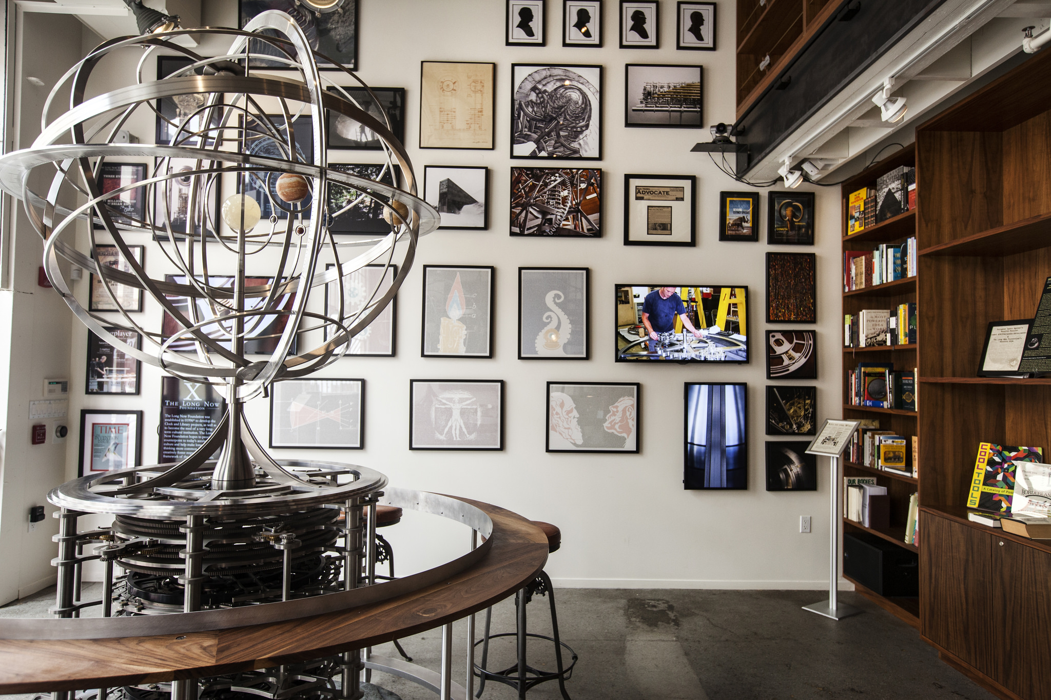  The stunning prototypes from the Clock of the Long Now like the Orrery,&nbsp;stand as a tall anchor at the entry. The two-story bookshelves beyond and the bar in the back draw people inside to this cozy space. 