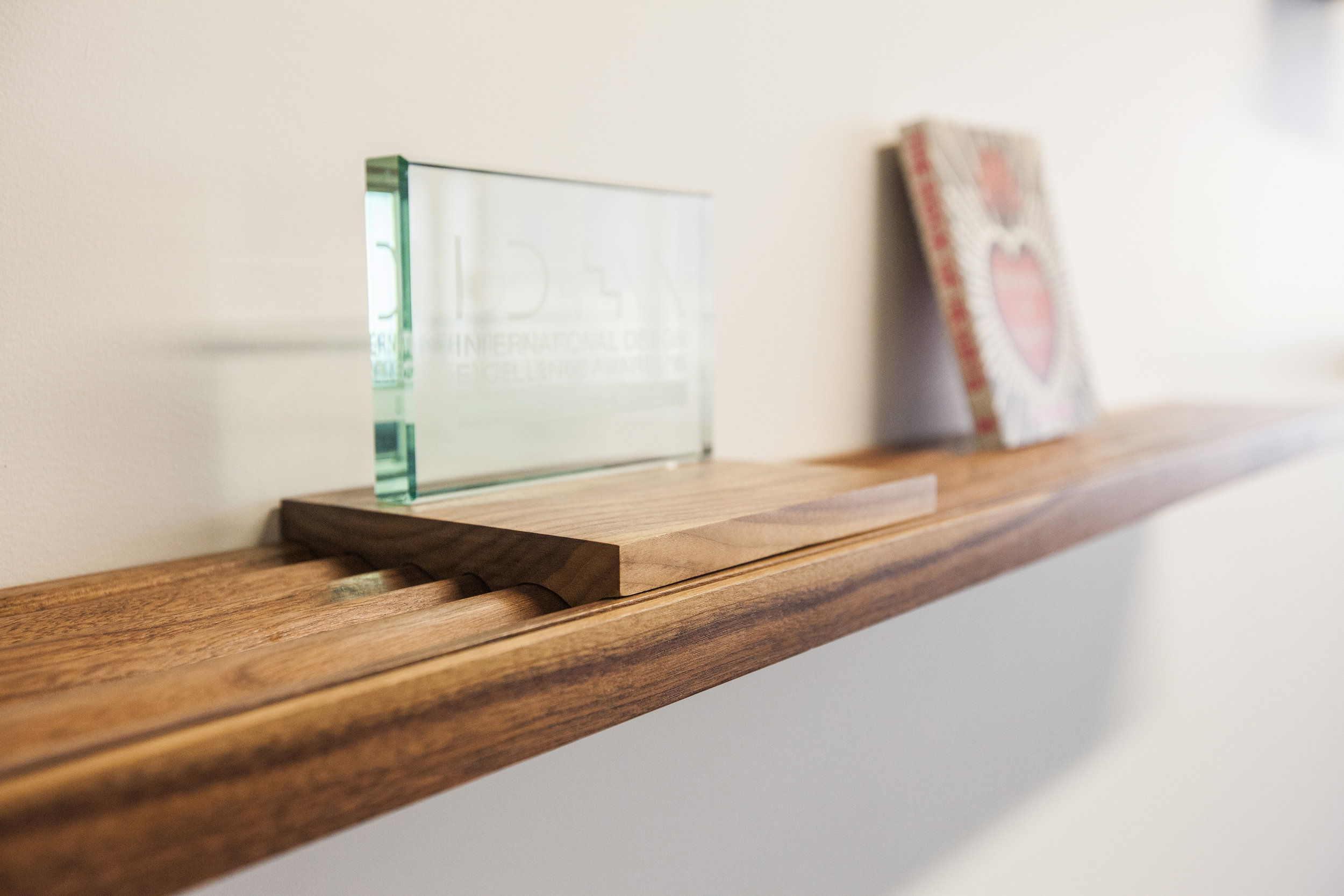  The grooves in the shelves allow for leaning different sizes of books, magazines and other printed materials. These small blocks carved with the same relief pattern sit on top the grooves and allow for awards and other items that need a flat surface