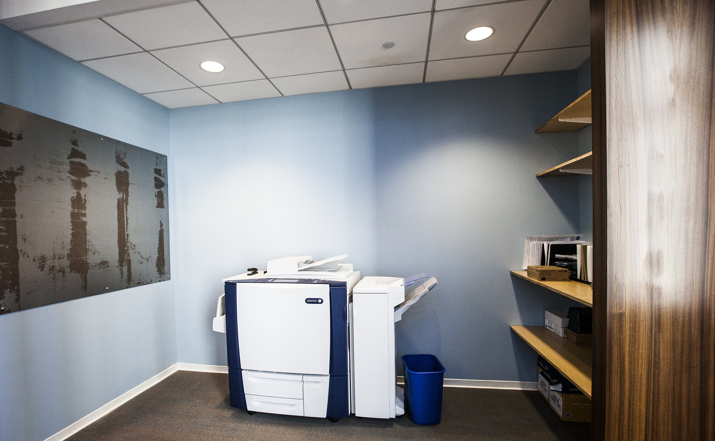 Even the tiny copy room has tones of the the office colors with wooden shelves, rusty metal and a sky blue wall.