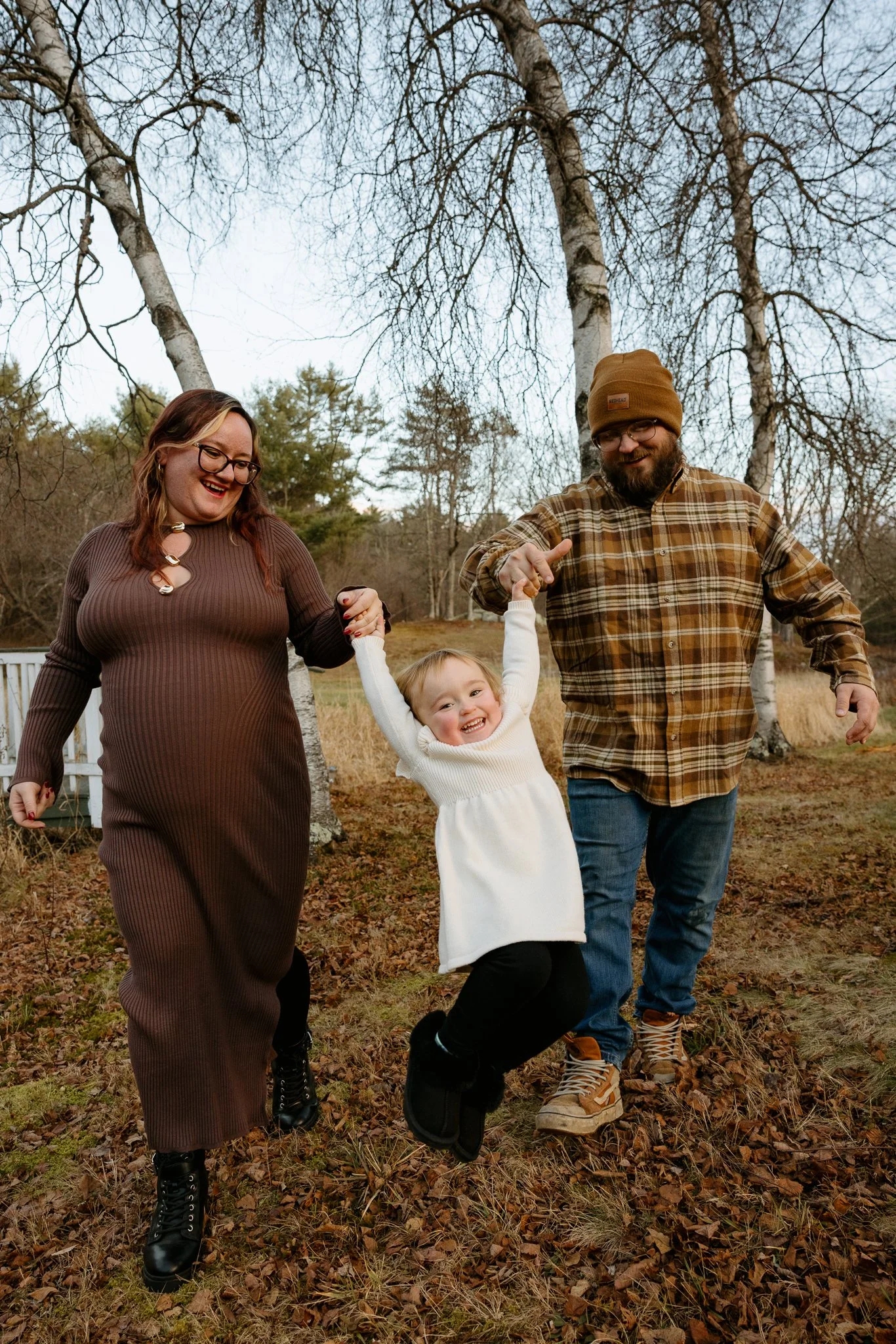 A family of four, including a mother, father, and two children, enjoying a walk outdoors in a wooded area during fall. They are holding hands and smiling.