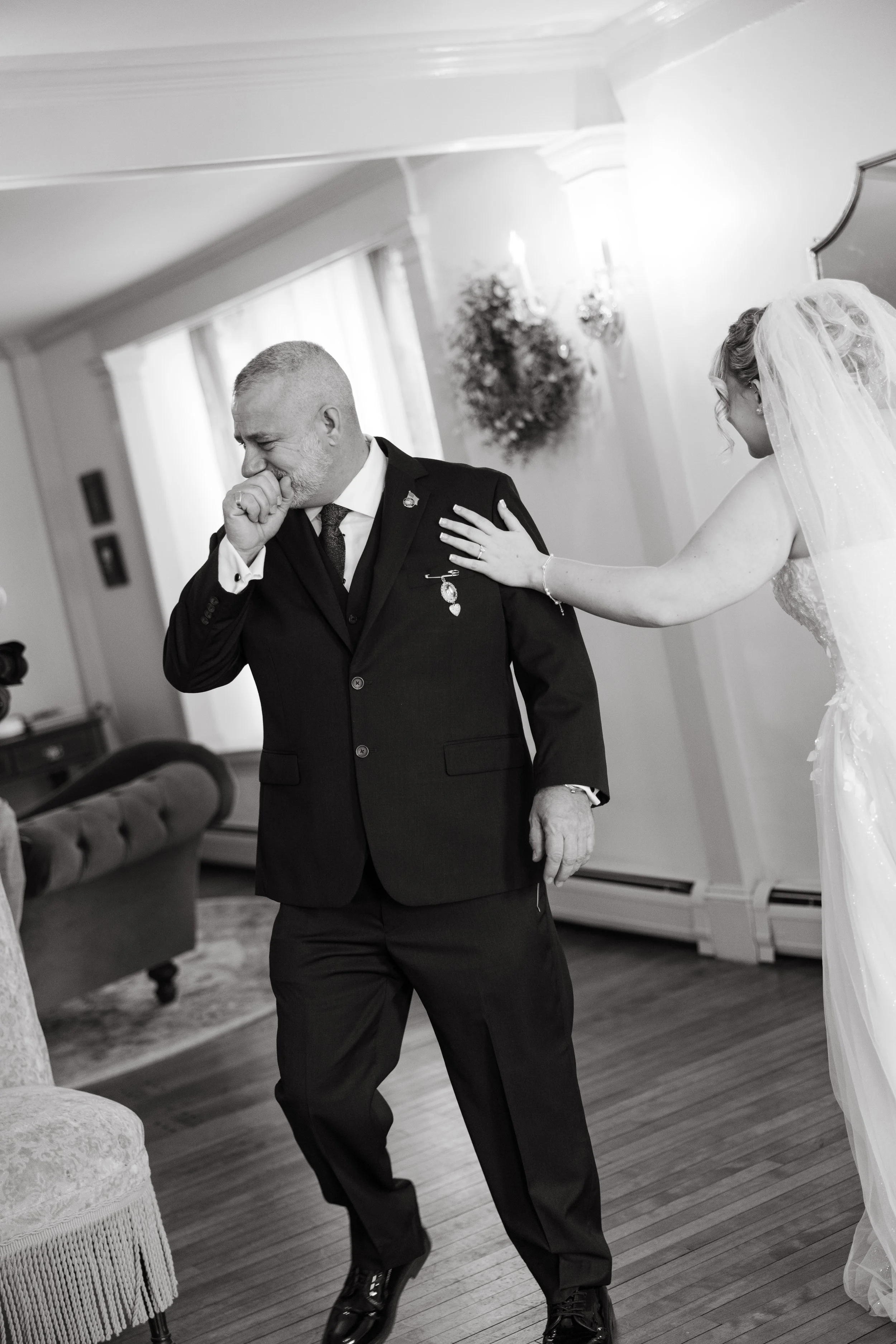 A black and white photo of a man in a tuxedo crying, possibly at a wedding, with a woman in a wedding dress and veil touching his shoulder.