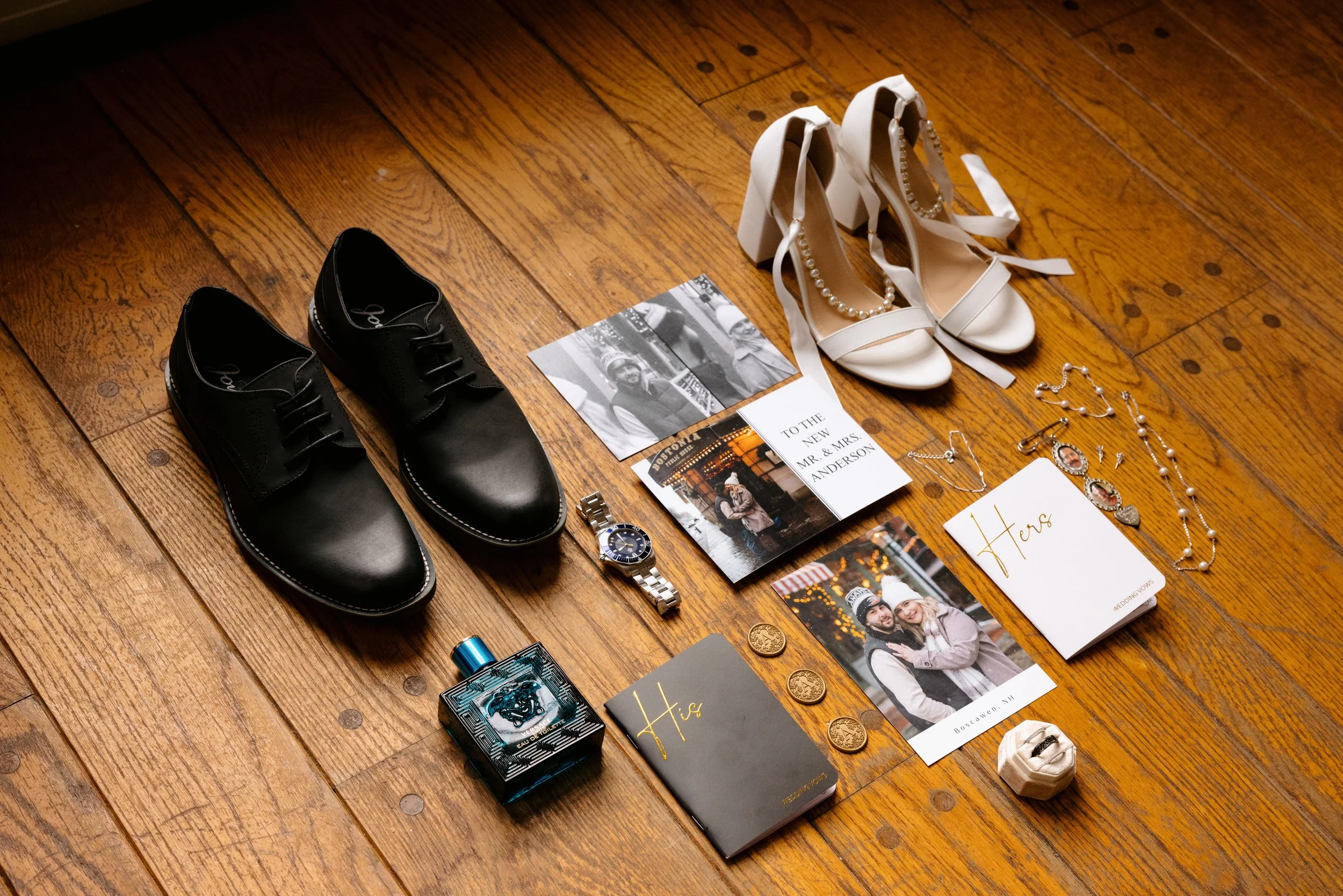 Collection of men's and women's shoes, jewelry, perfume, and personal items on wooden floor, including black dress shoes, white high heels with pearl accents, jewelry, a wristwatch, a wedding photo, and a greeting card.