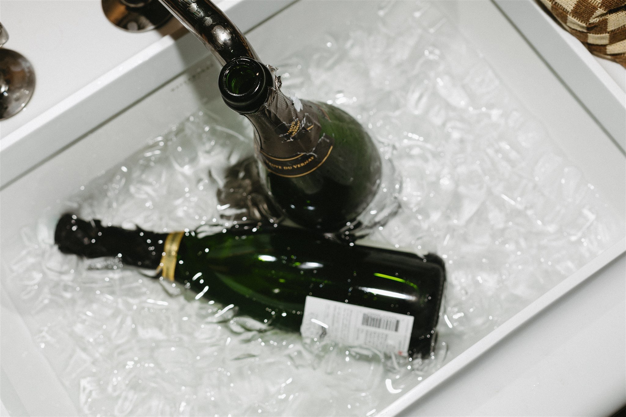 Two champagne bottles chilling in a white tray filled with ice.