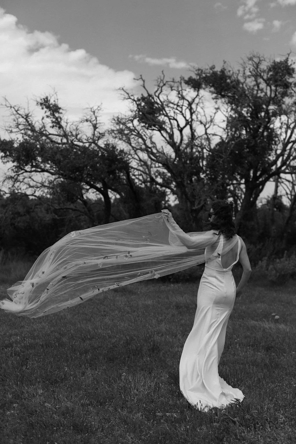 A woman in a long dress standing in a field with trees. Brides. Grooms. Bride and Groom. Couples. Weddings. Lifestyle. Family. Friends. Festivals. Wedding Photographer. Austin Wedding Photographer. Traveling photographer. Luxury photographer.