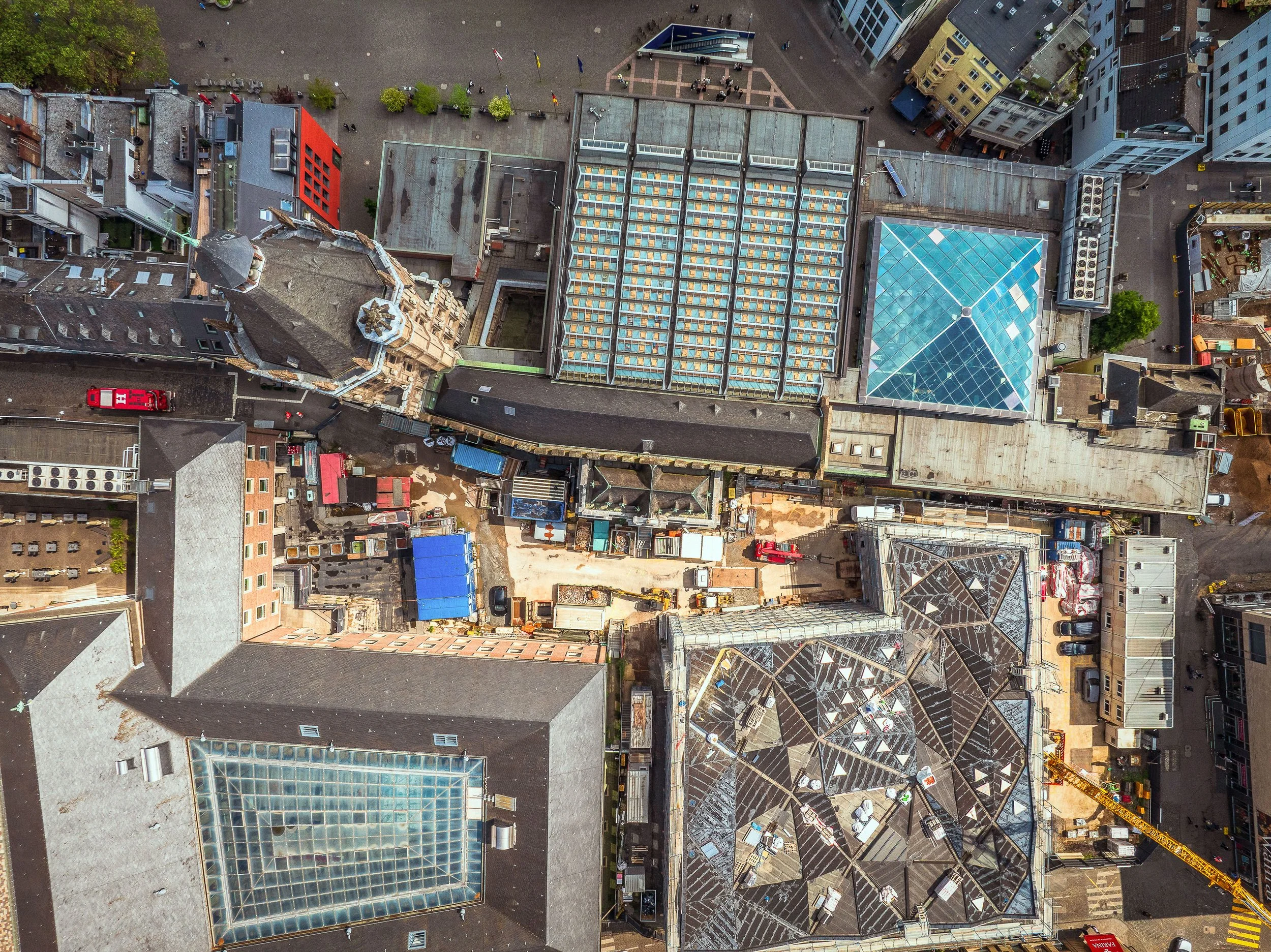 Senkrechte Luftaufnahme des Kölner Rathausplatzes mit einer Baustelle zwischen den Gebäuden des Historischen Rathauses. Zu sehen sind Baugeräte, Container und Gerüste sowie die umliegenden Dächer.