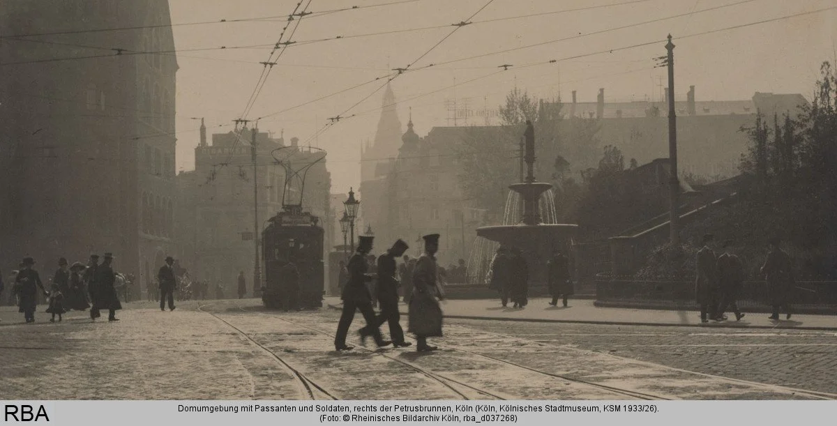 Historische Aufnahme der Domumgebung mit Straßenbahn, Passant*innen und dem Petrusbrunnen auf der rechten Bildseite.