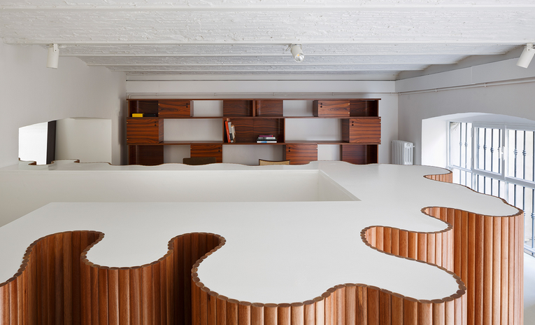 The space features an undulating wooden screen that acts as a hidden staircase that cuts through the building's two floors